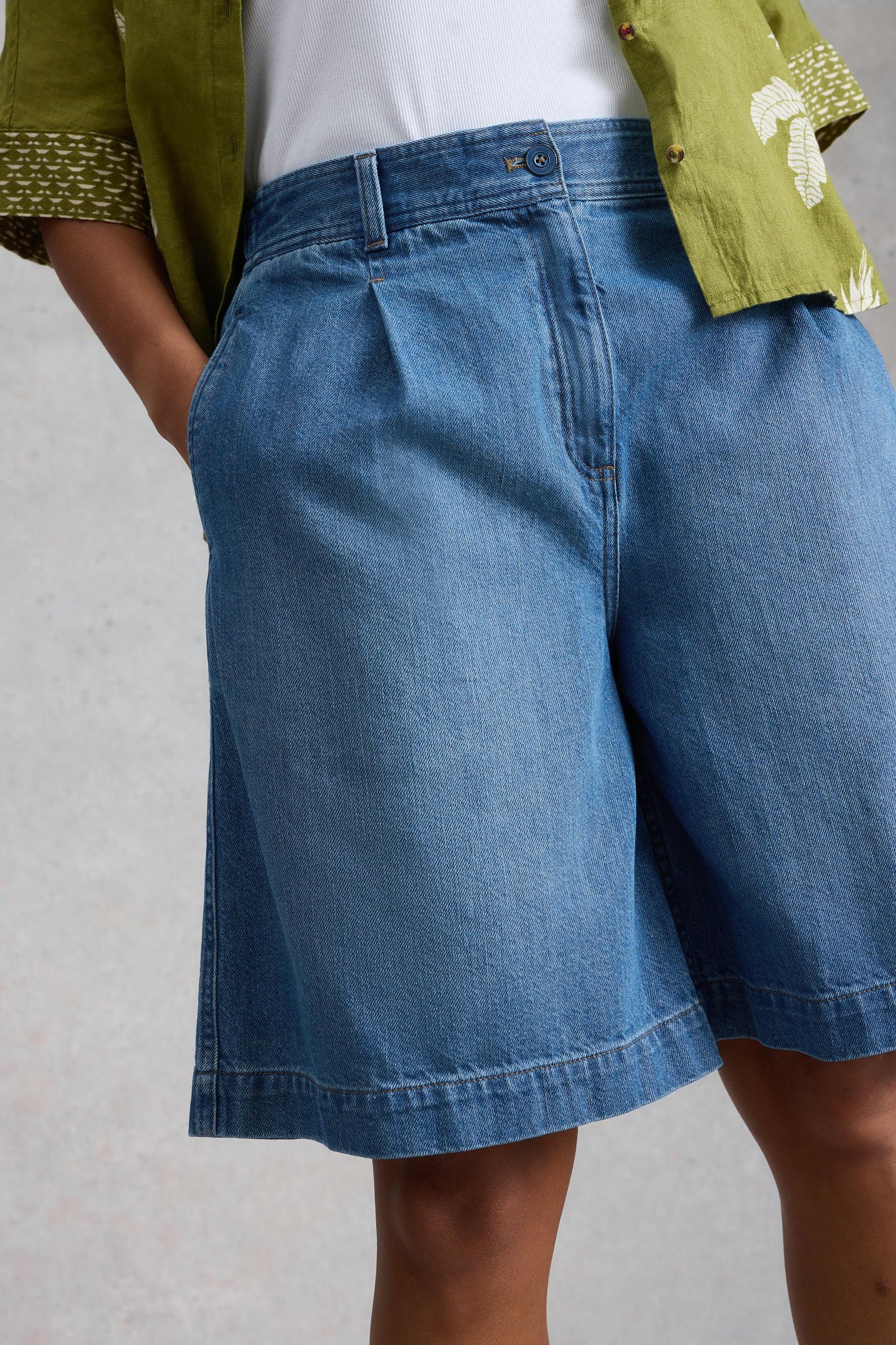 Person wearing blue denim shorts with a plain background