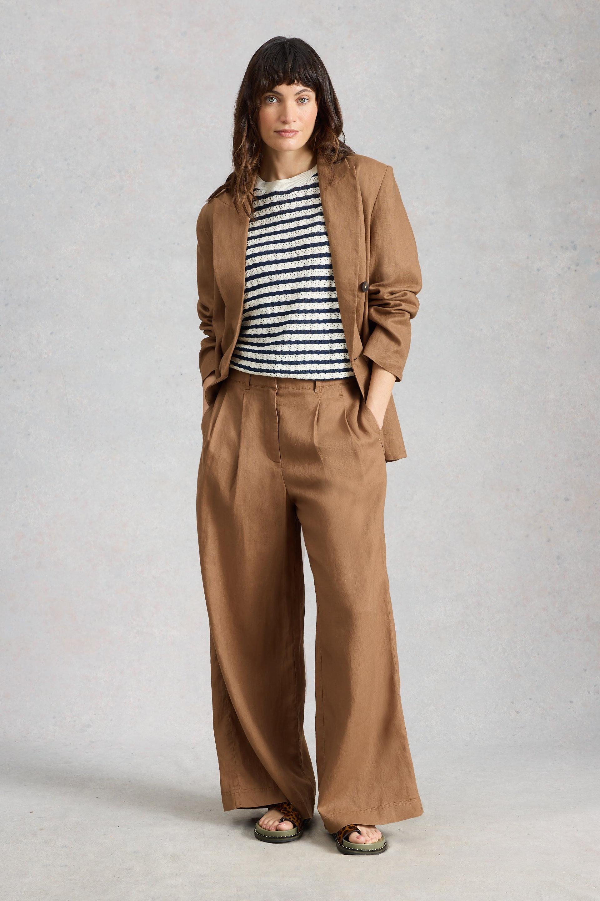 Woman wearing a brown linen suit with a striped shirt on a plain background