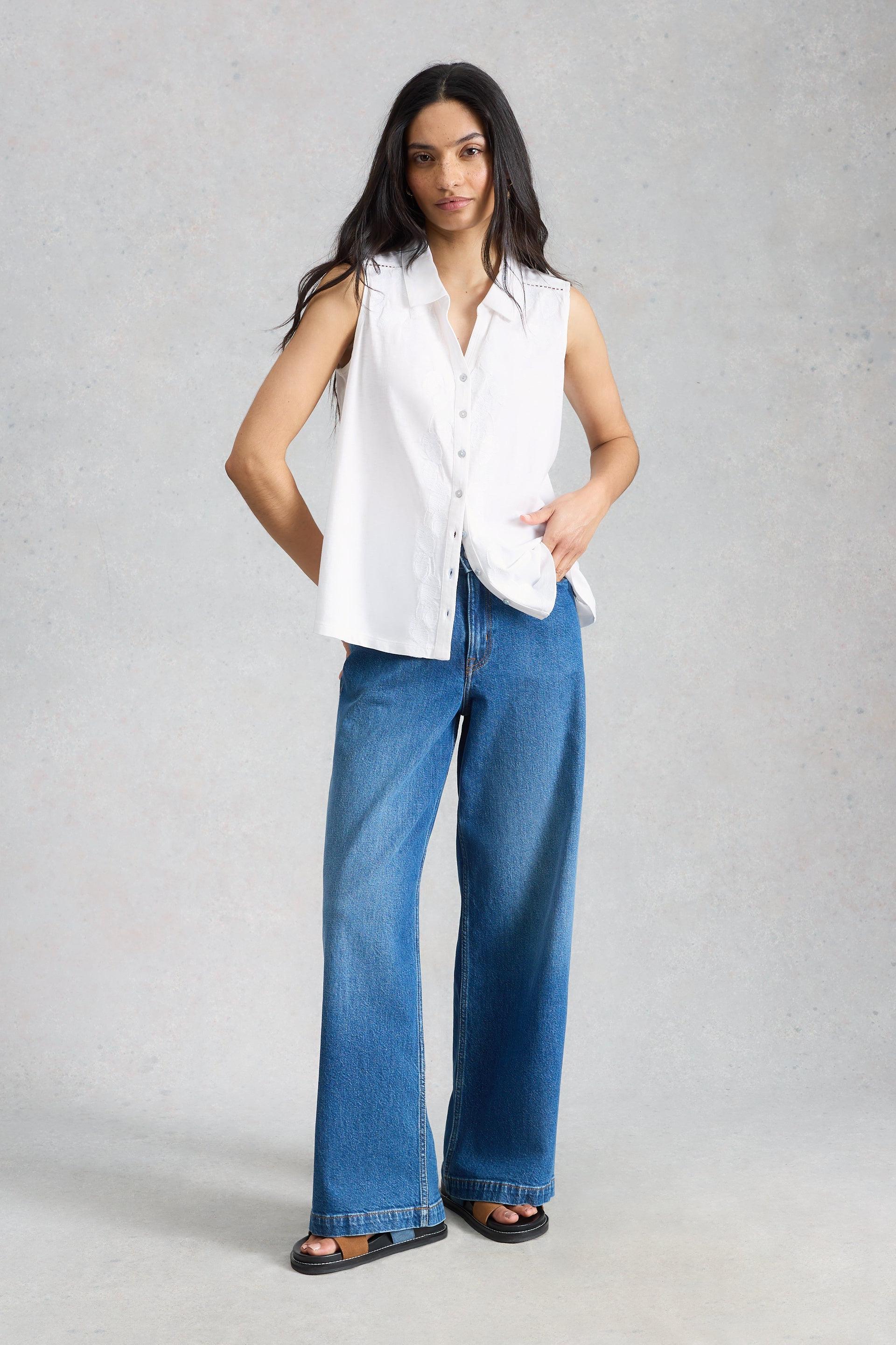 Woman wearing a white sleeveless blouse and blue jeans on a gray background