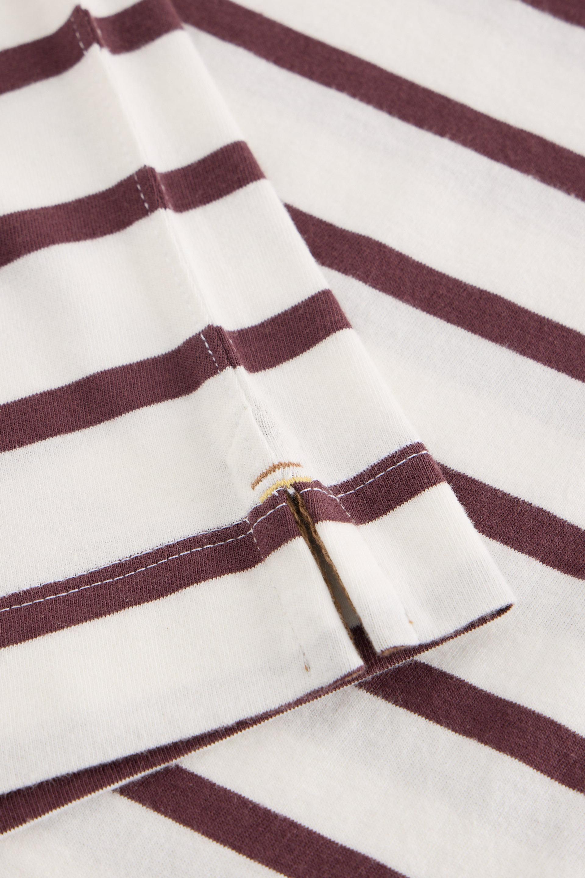 Close-up of a striped fabric garment, showing alternating white and dark burgundy horizontal stripes with a folded cuff revealing contrast stitching.