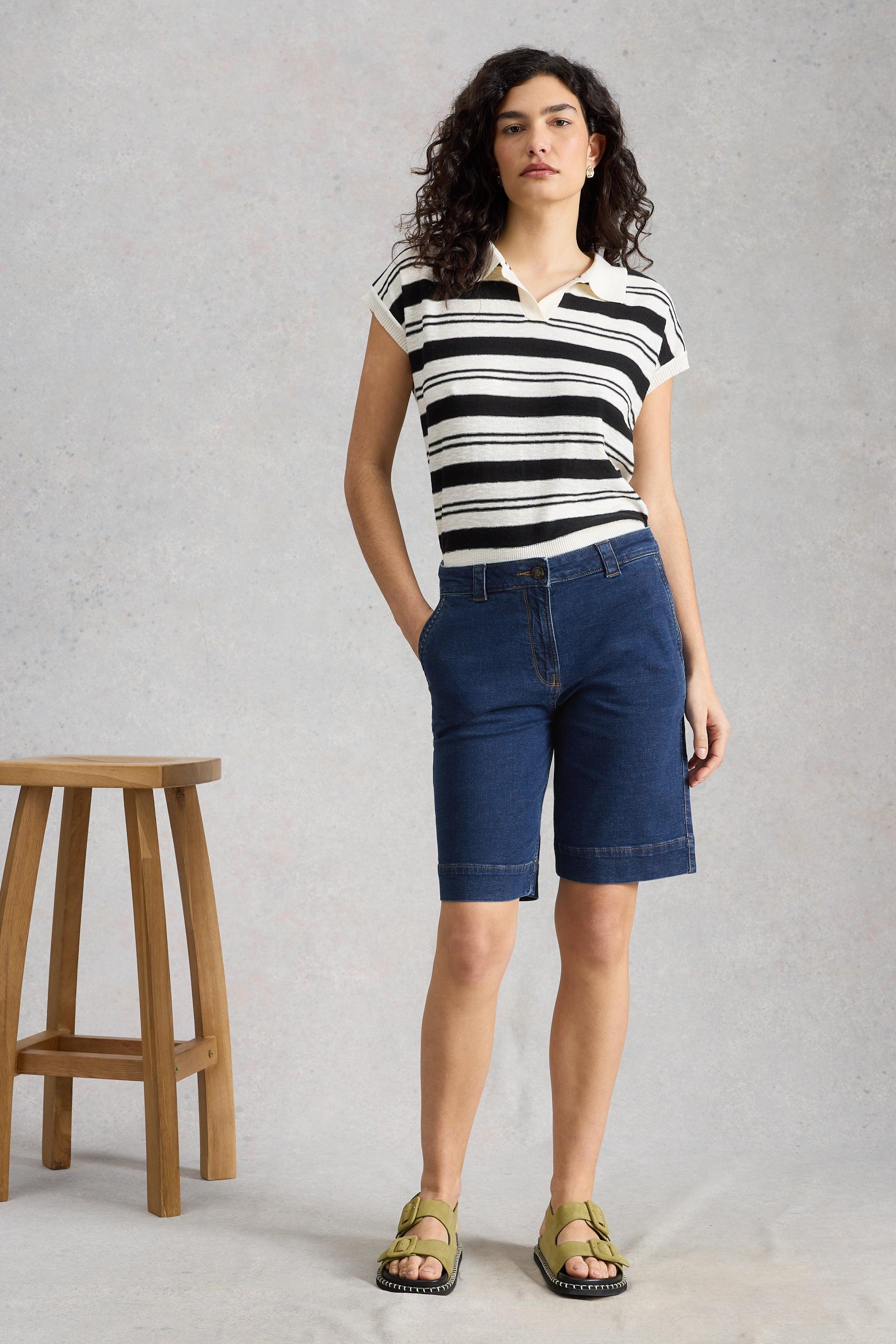 Woman wearing a black and white striped shirt and dark blue organic cotton shorts standing against a gray background.