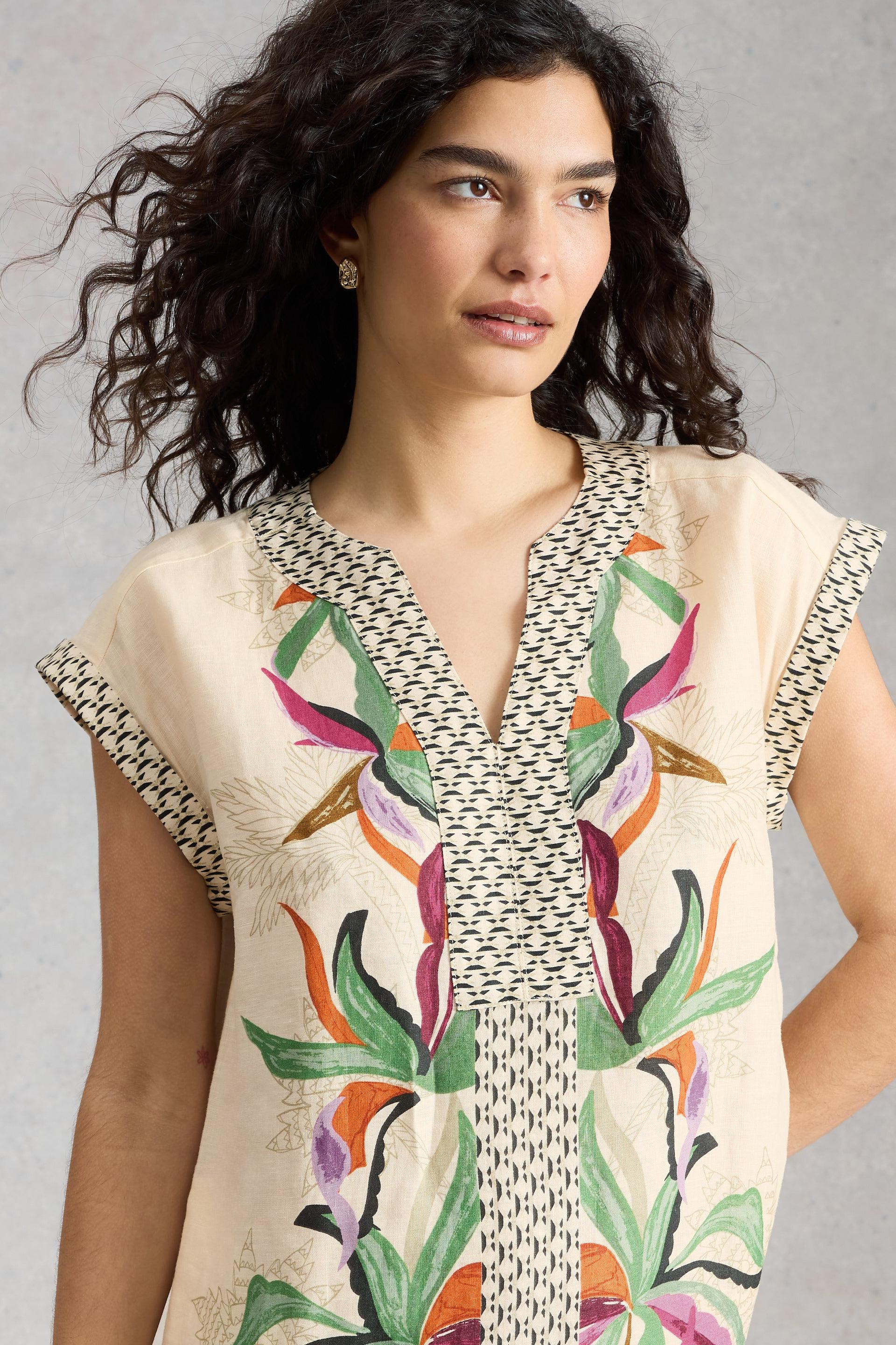 Woman wearing a sleeveless dress with colourful floral pattern against a gray background