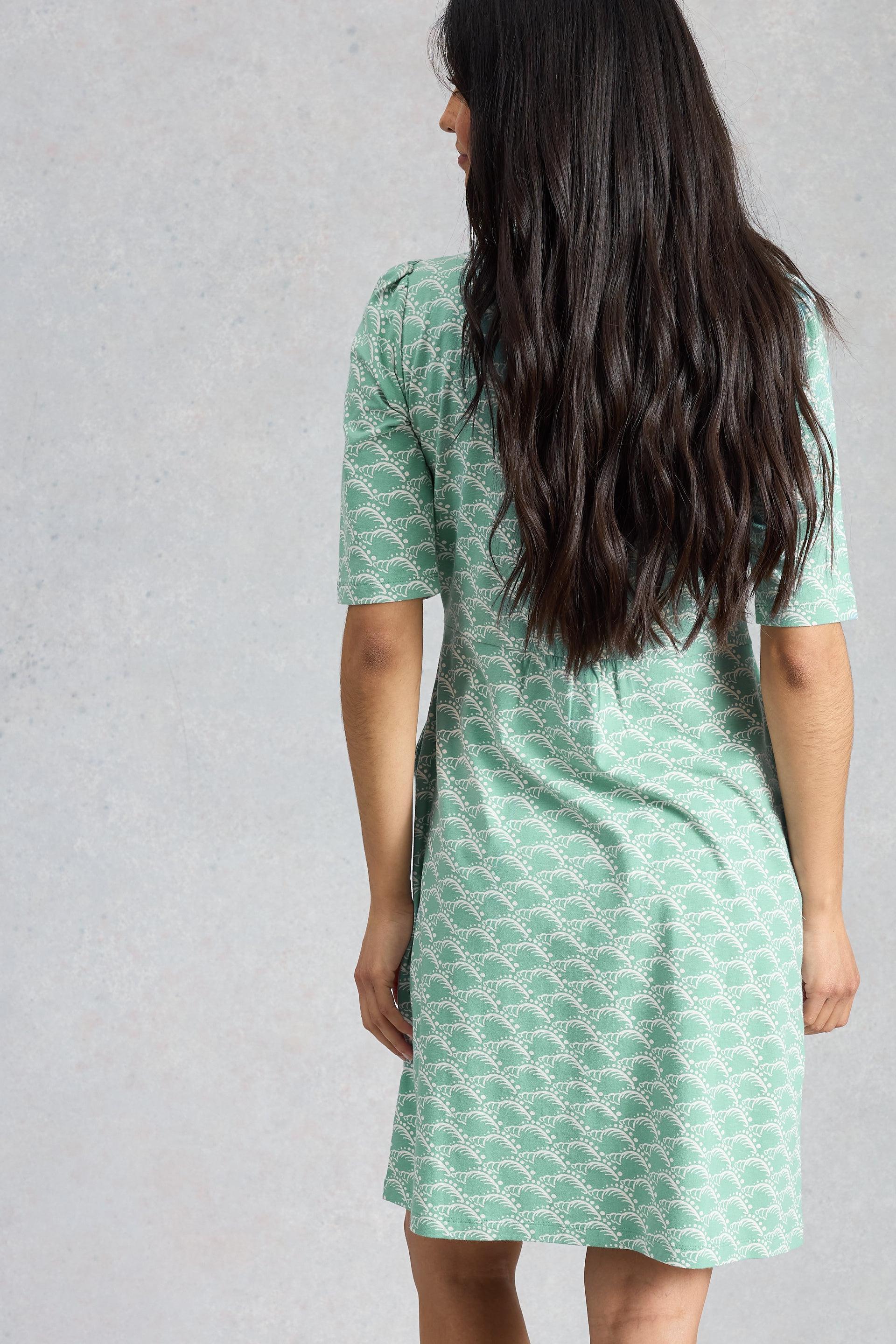 Woman wearing a green printed organic cotton dress against a gray background