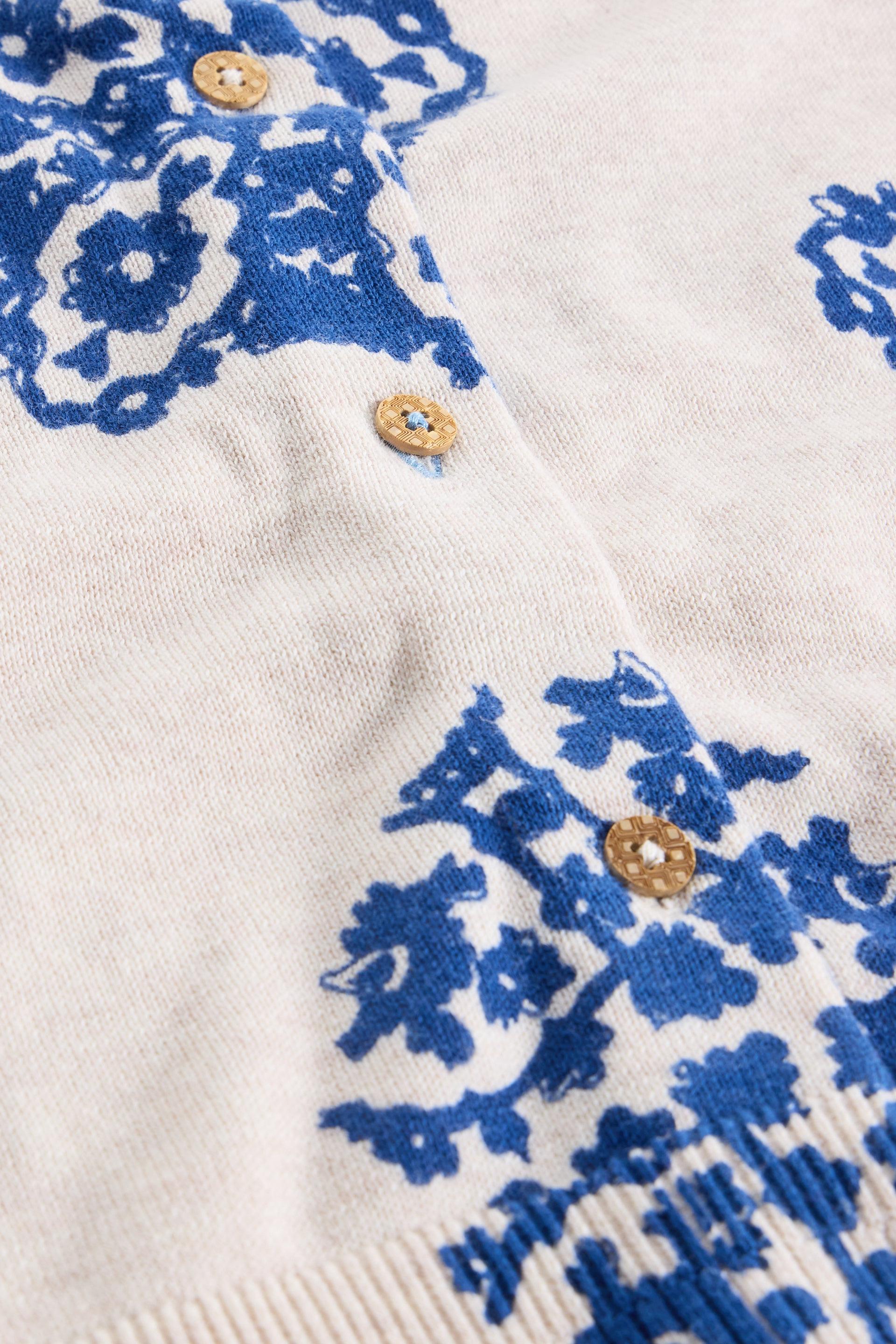 Close-up of a white organic cotton cardigan with blue floral patterns and gold buttons.