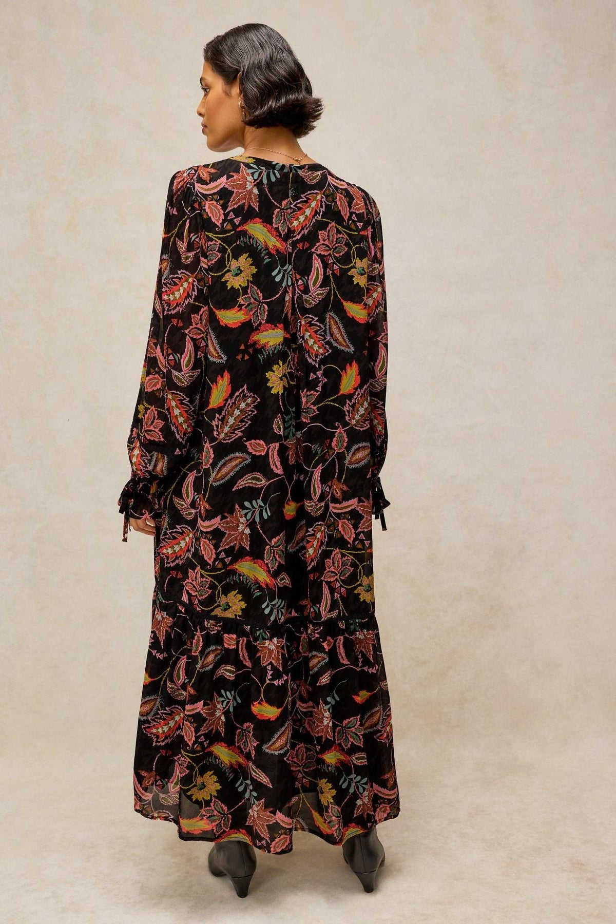 A woman wearing a black long-sleeved floral viscose maxi dress by White Stuff, viewed from behind.