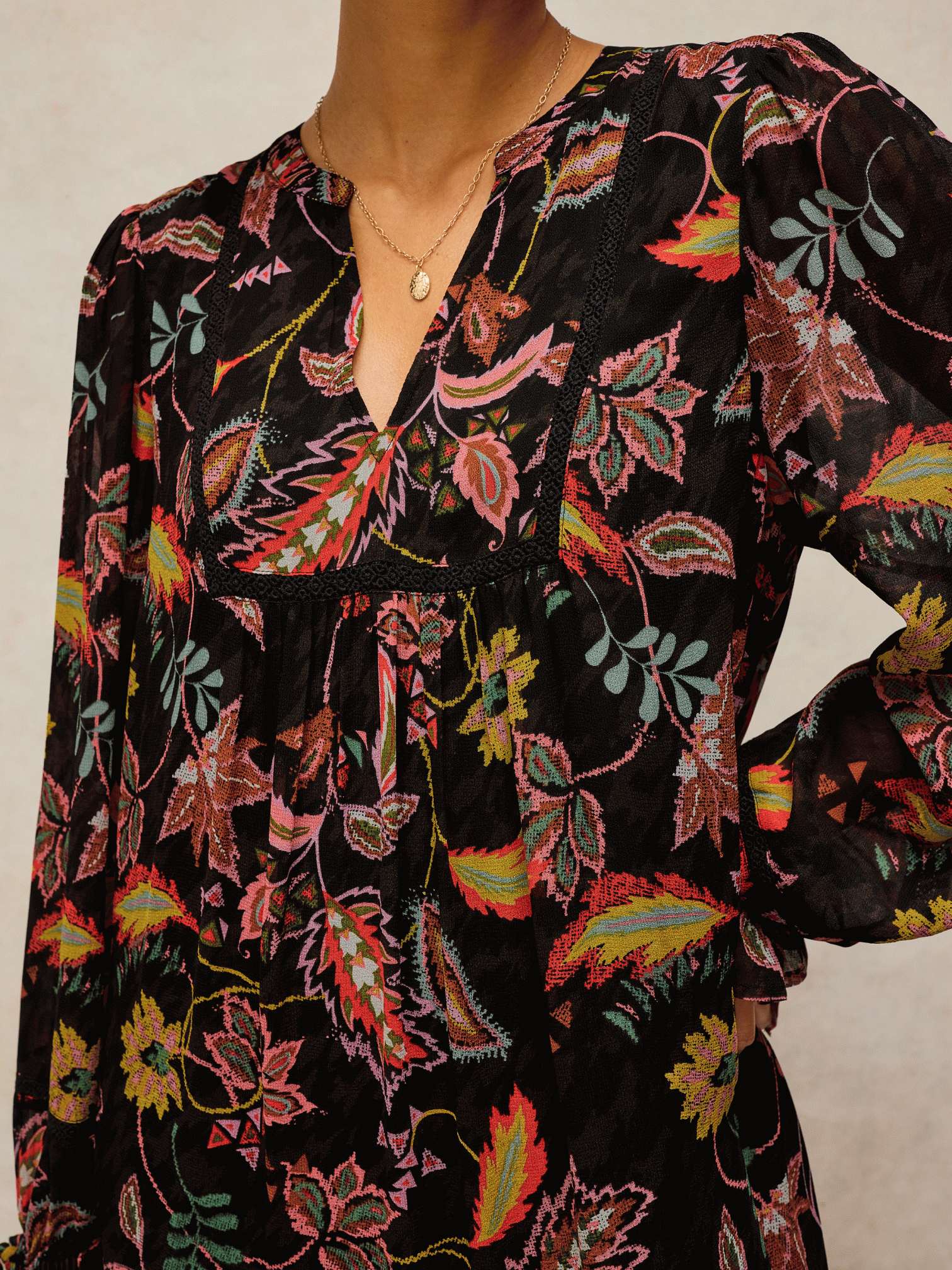 Close-up of a person wearing a black long-sleeved viscose dress with a vibrant, multi-colored floral paisley print.