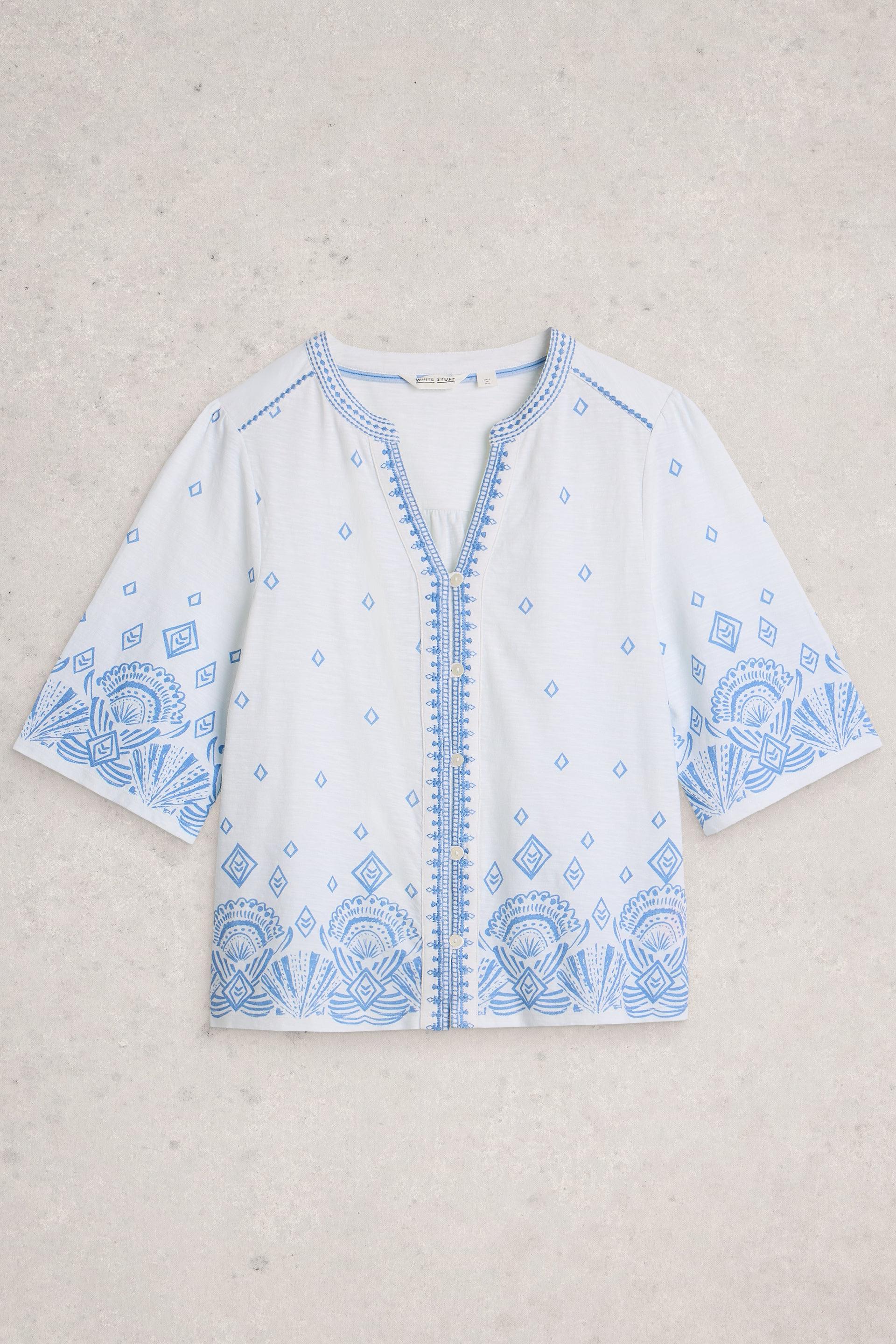 White organic cotton top with blue embroidery on a light gray background