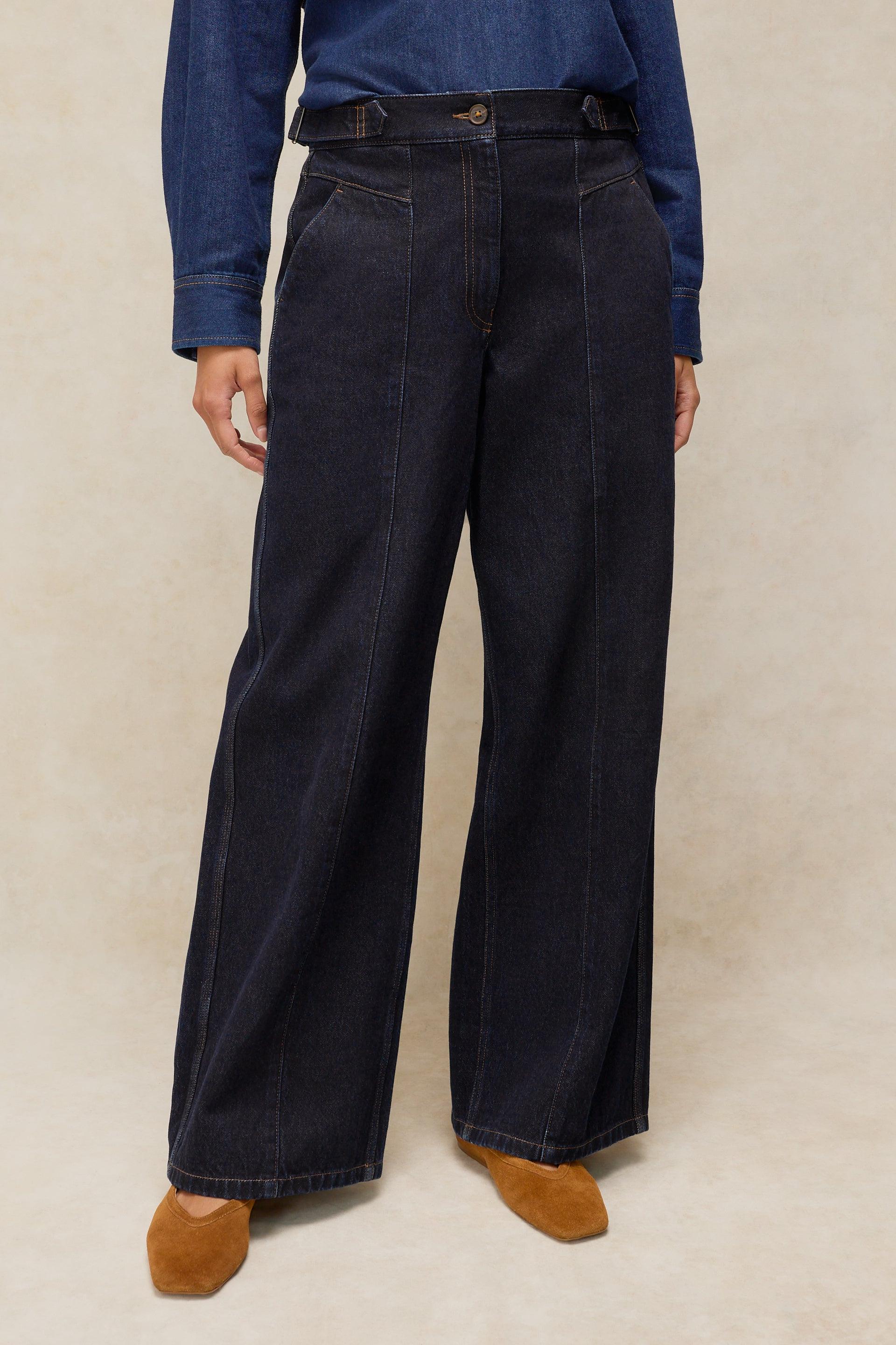 A person wearing dark indigo wide-leg denim trousers made from organic cotton by White Stuff.
