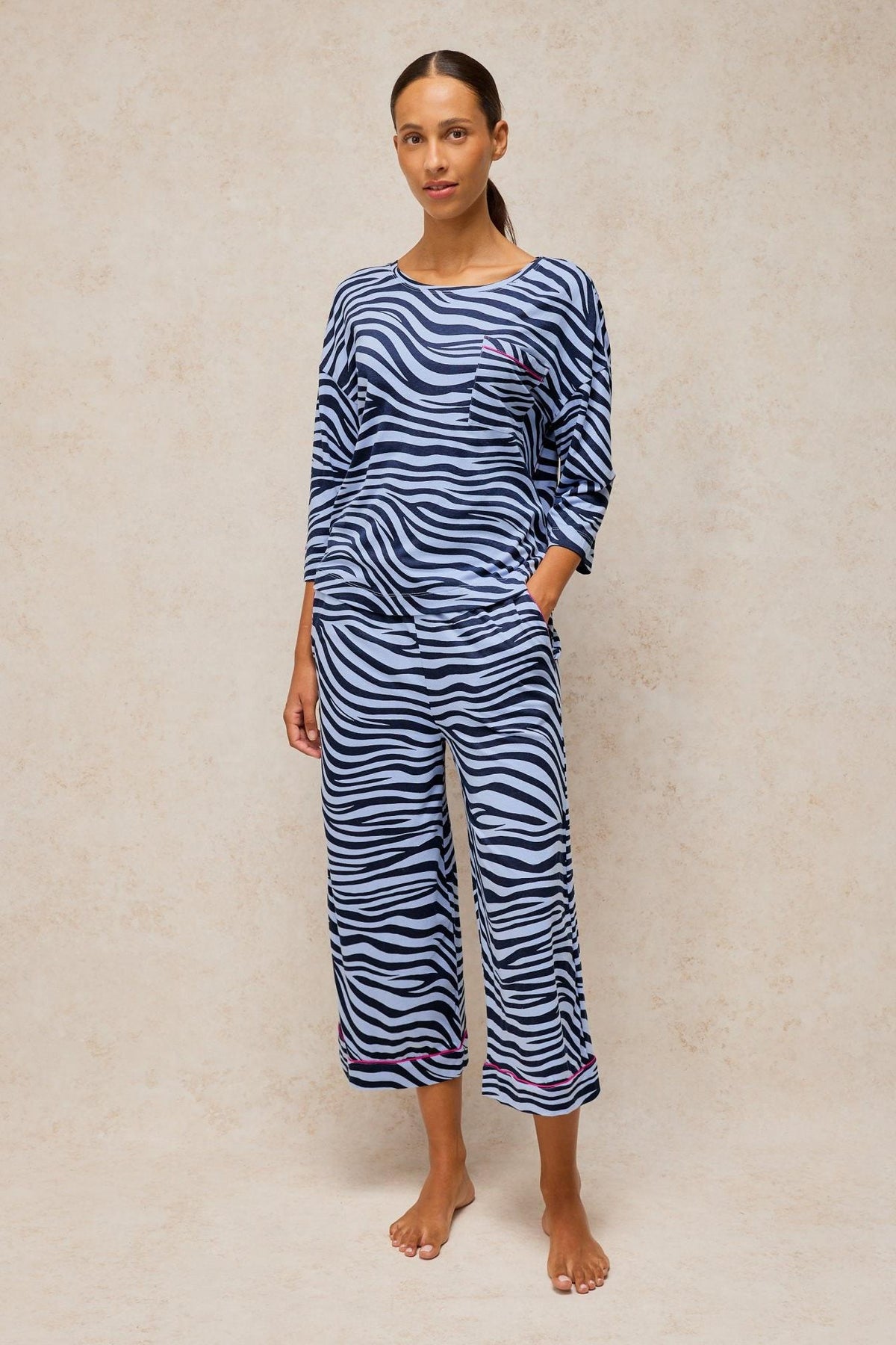 A woman modeling a blue animal print White Stuff pyjama top and matching trousers against a neutral background.