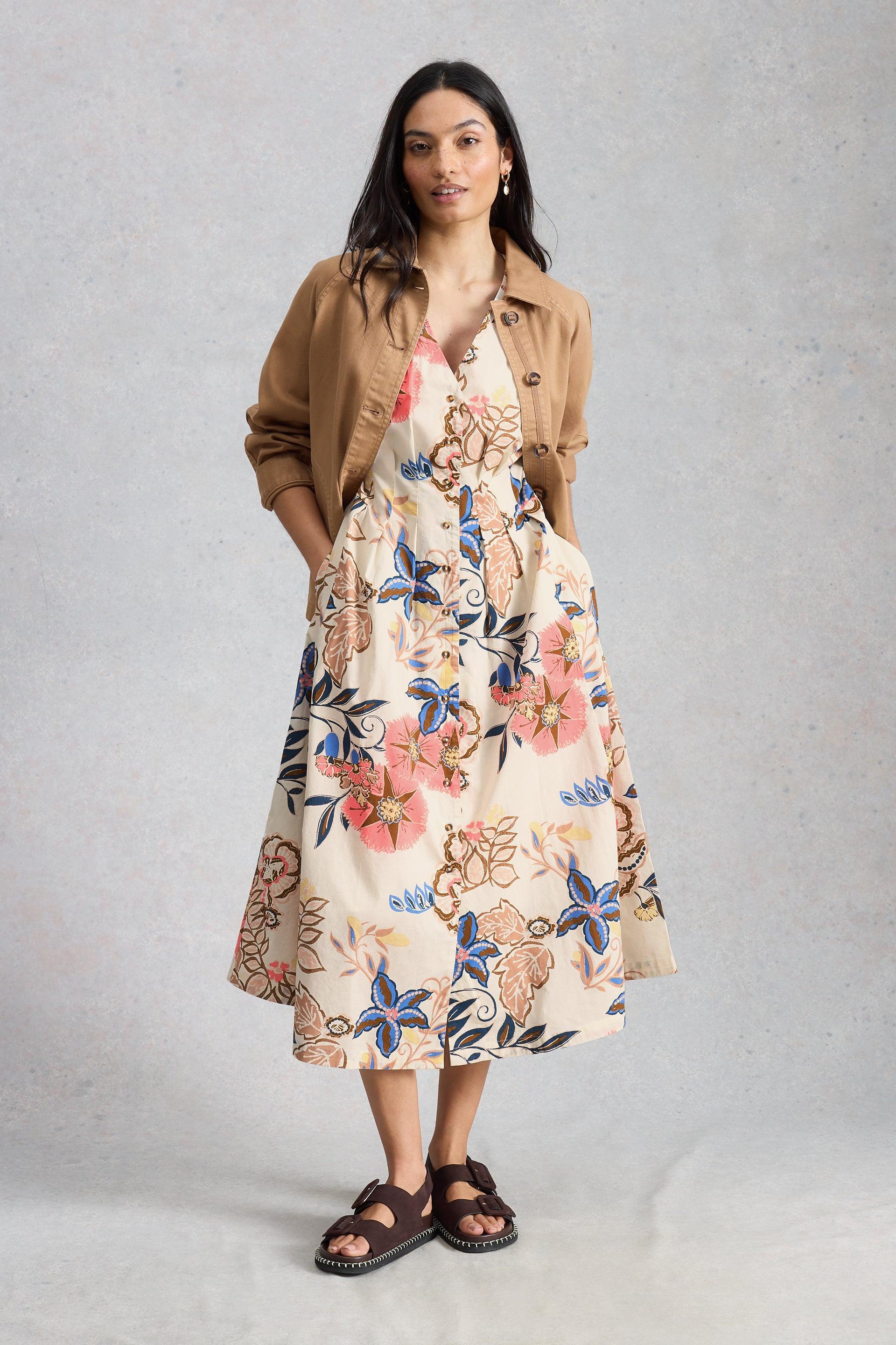 Woman wearing a floral organic cotton midi dress with a brown jacket against a gray background