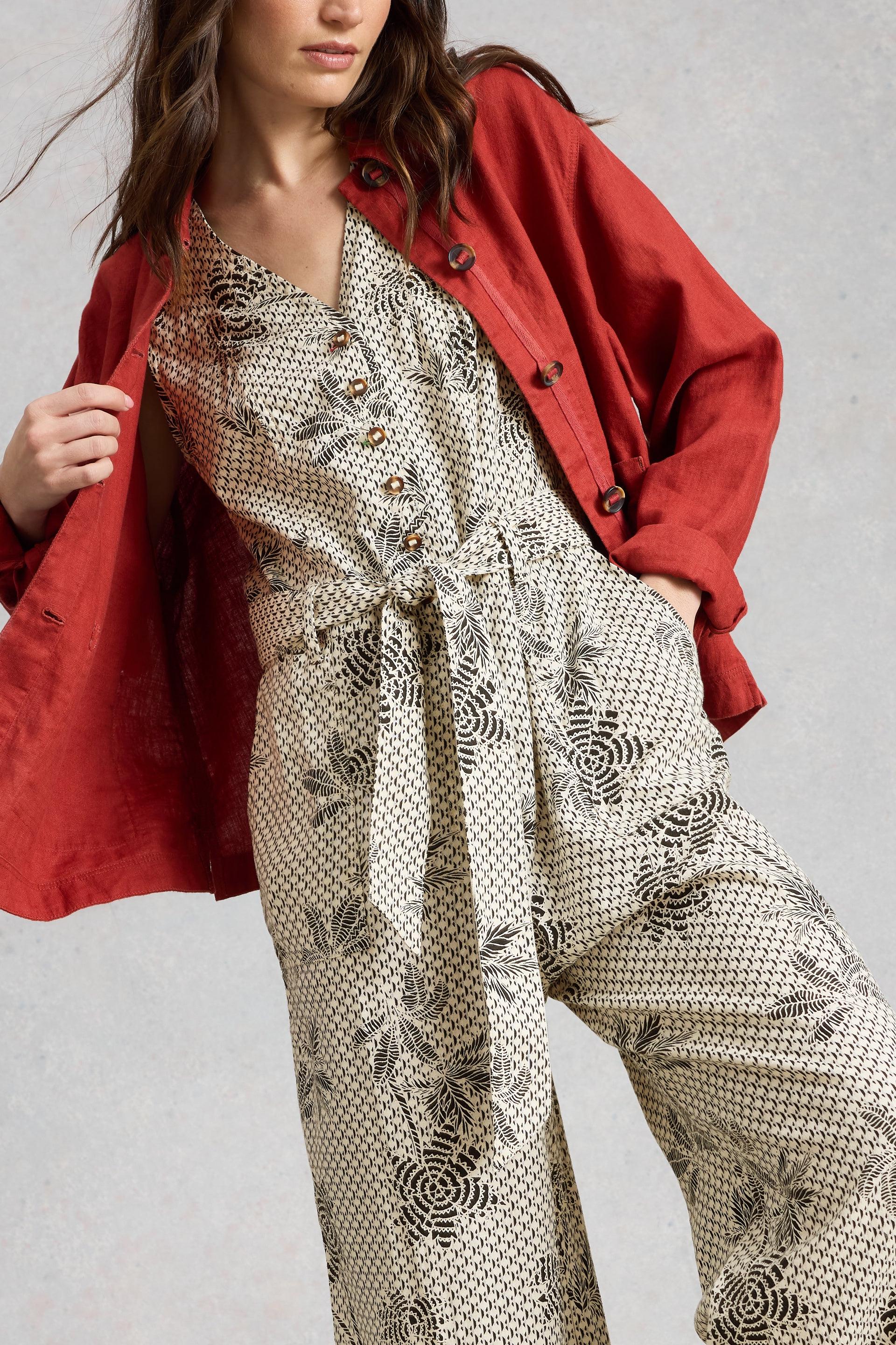 Person wearing a red jacket over a patterned White Stuff jumpsuit on a plain background