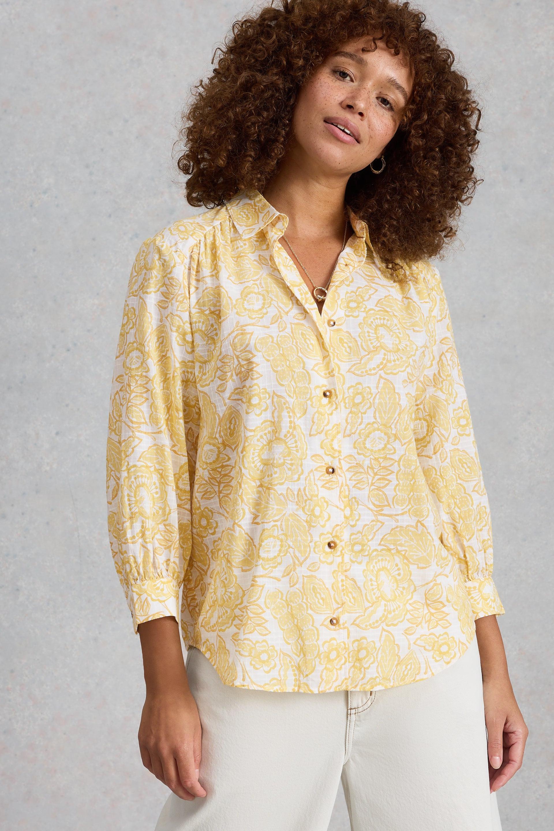 Woman wearing a White Stuff yellow floral blouse against a gray background