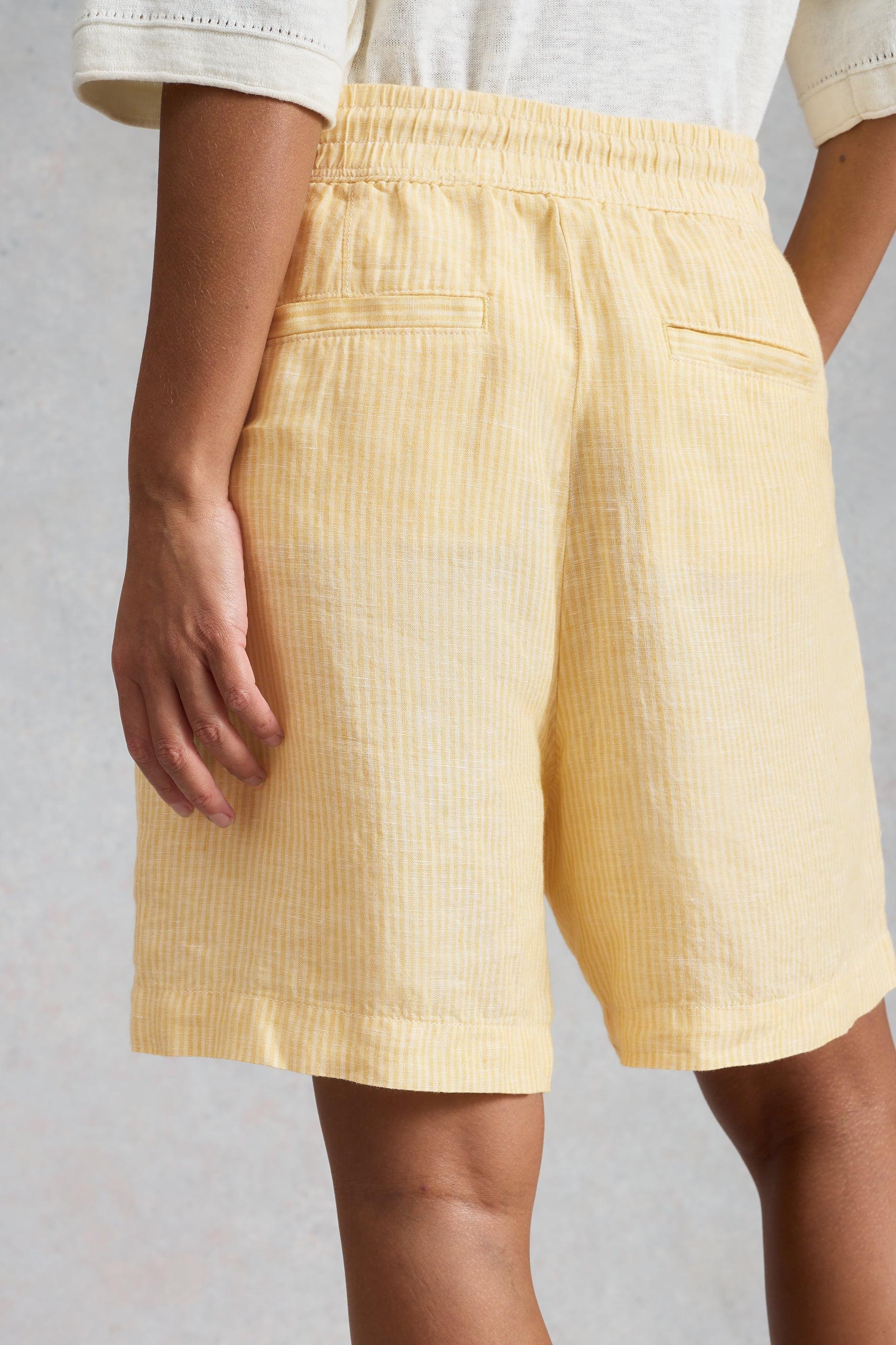 Yellow linen shorts with two back pockets worn by a person on a plain background