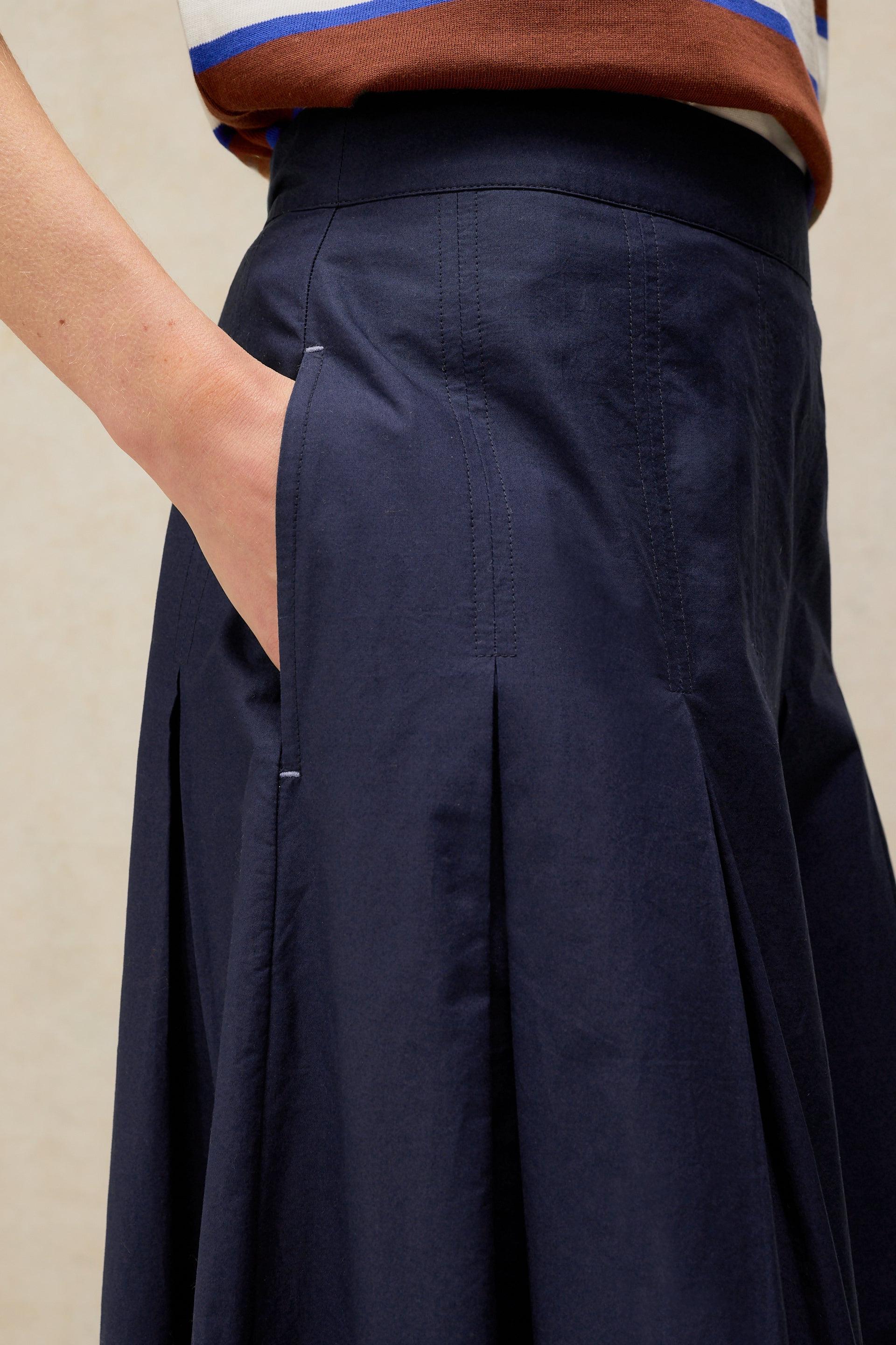 A close-up view of a person wearing a navy blue pleated skirt made from organic cotton with a side pocket