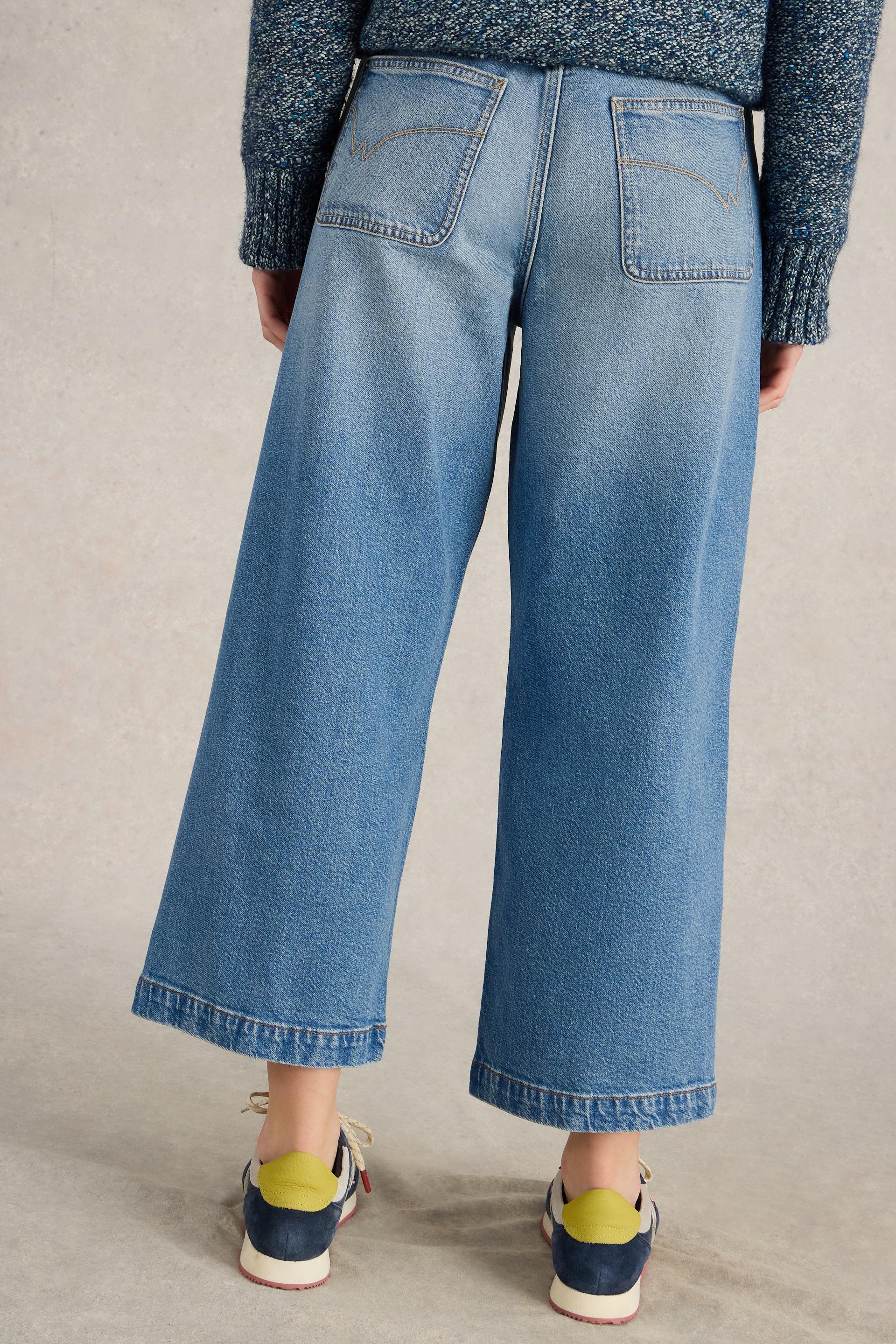 A person wearing wide-leg blue jeans made of organic cotton paired with a blue textured sweater and sneakers