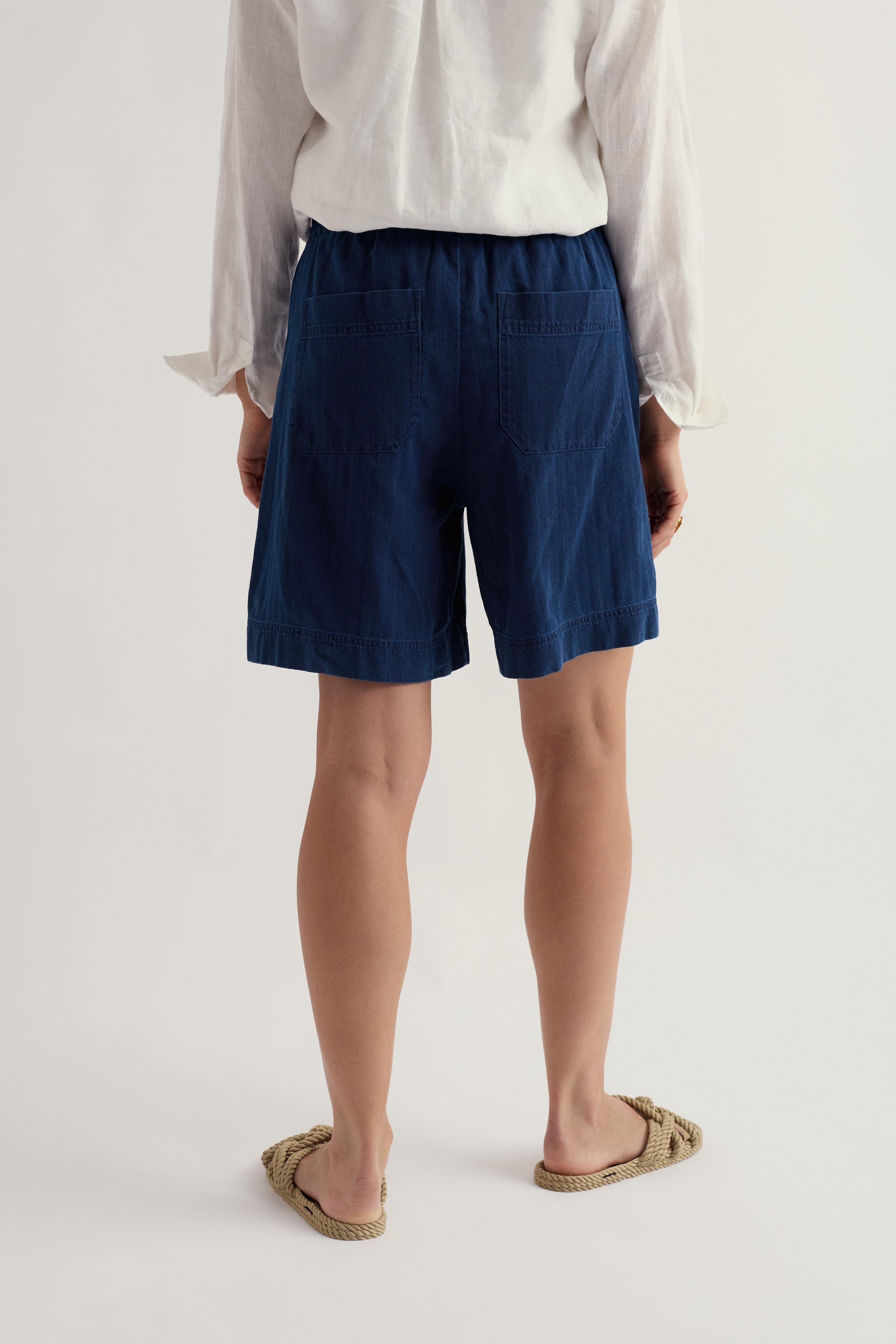 Person wearing navy organic cotton shorts and a white shirt on a plain background