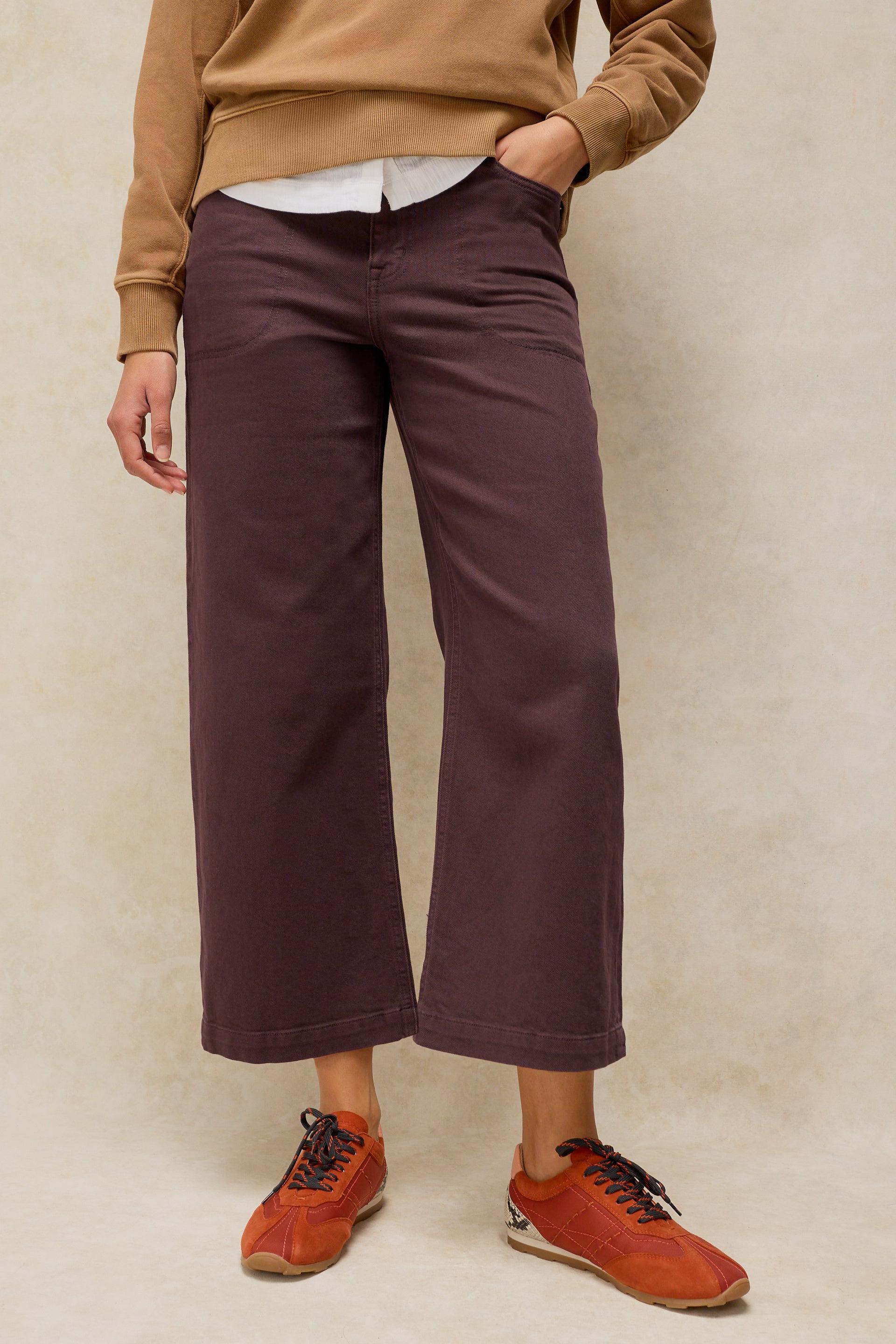 A person wearing brown wide-leg trousers and orange sneakers against a neutral background