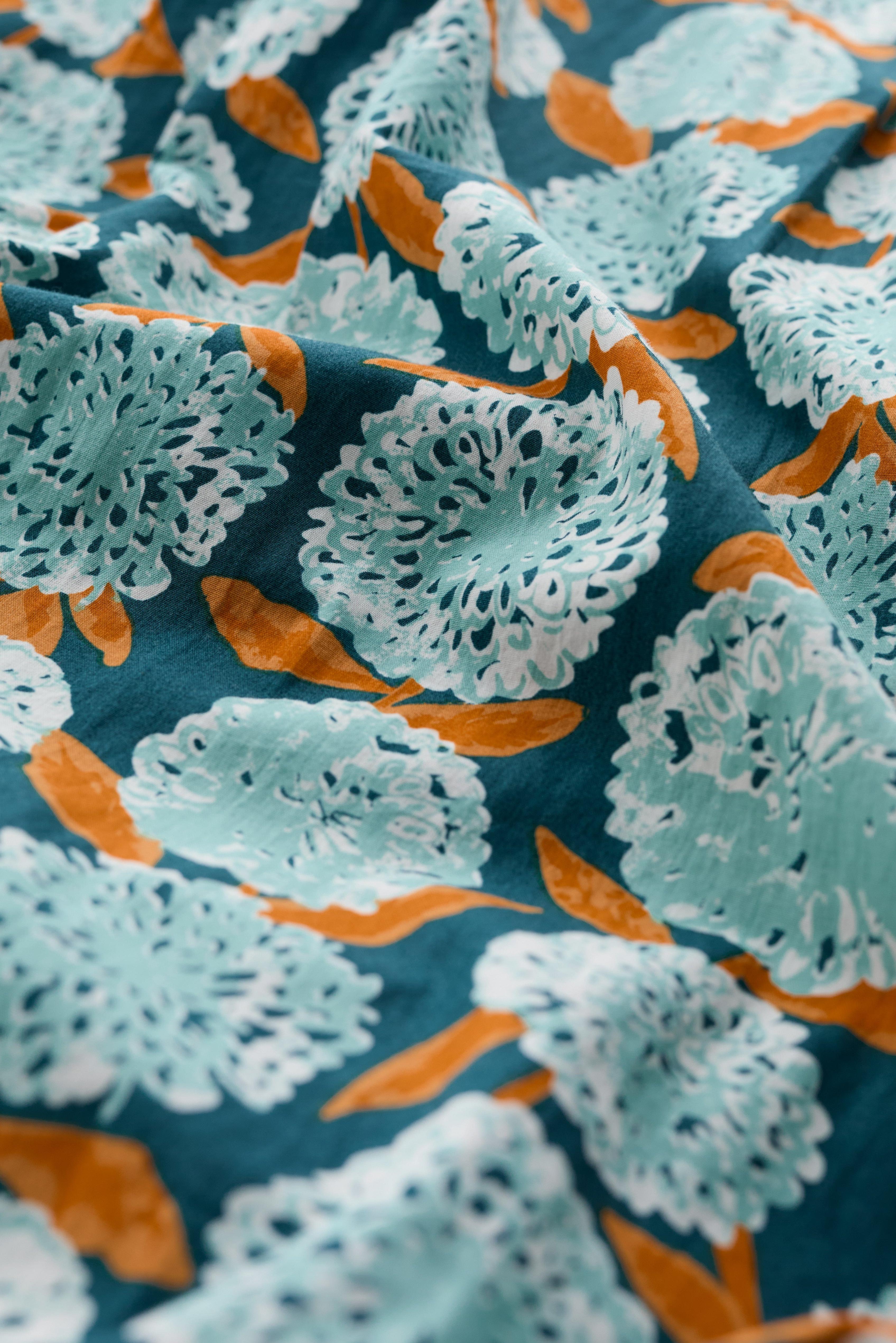 Close-up of a fabric with a floral pattern featuring light blue flowers and orange leaves on a dark blue background.