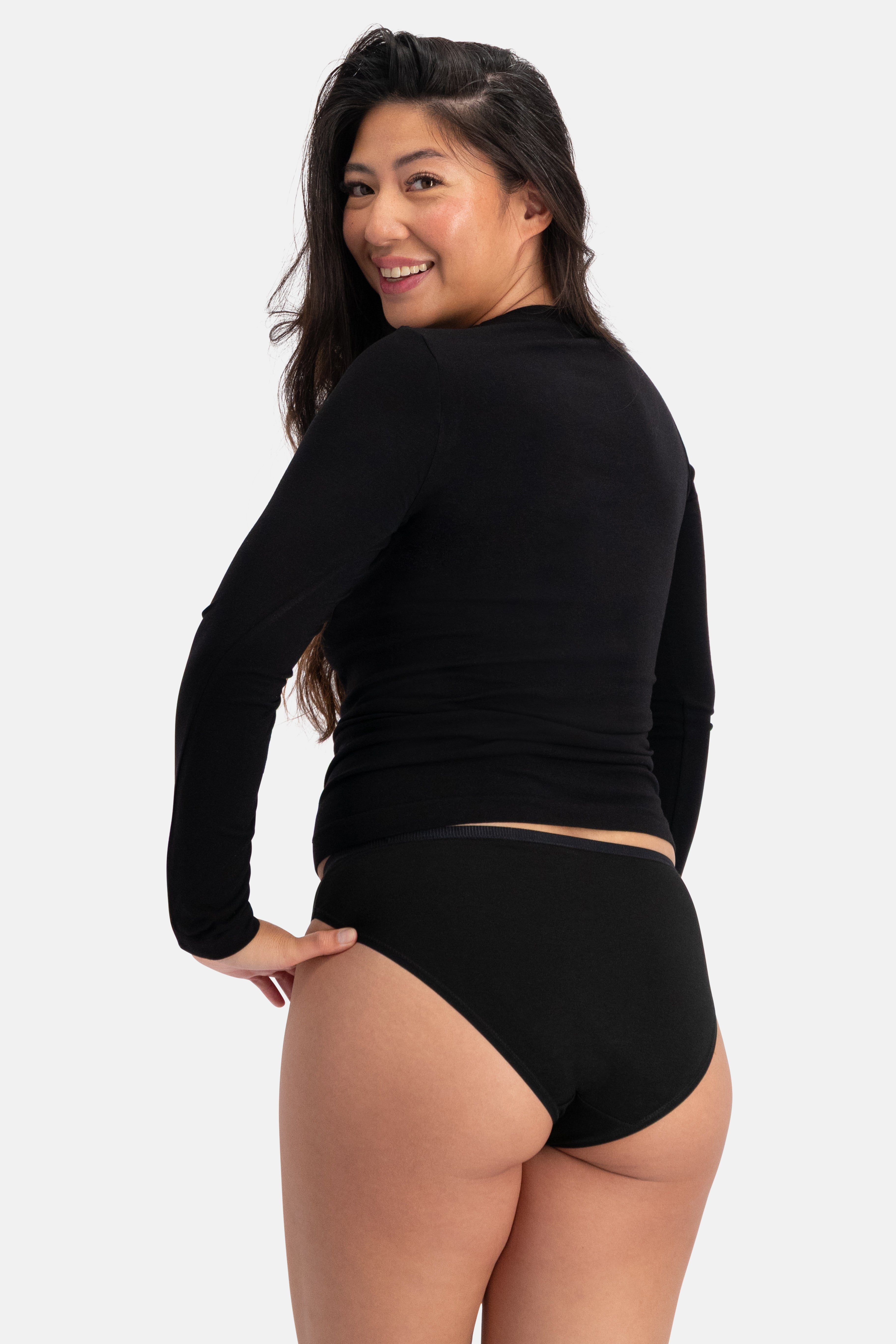 Asian woman smiling, wearing black long-sleeve shirt and black bamboo fabric briefs, looking over her shoulder