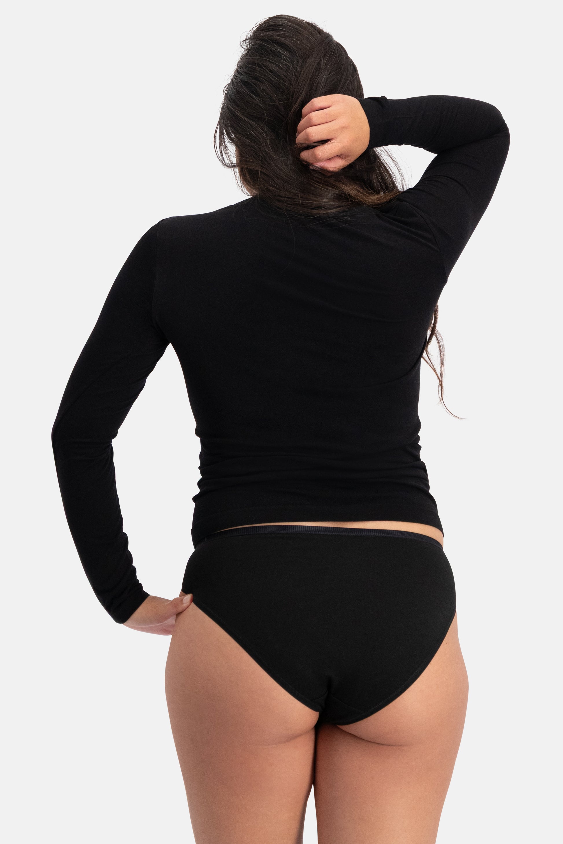 Rear view of a woman with long dark hair wearing a black long-sleeve top and black bamboo fabric underwear