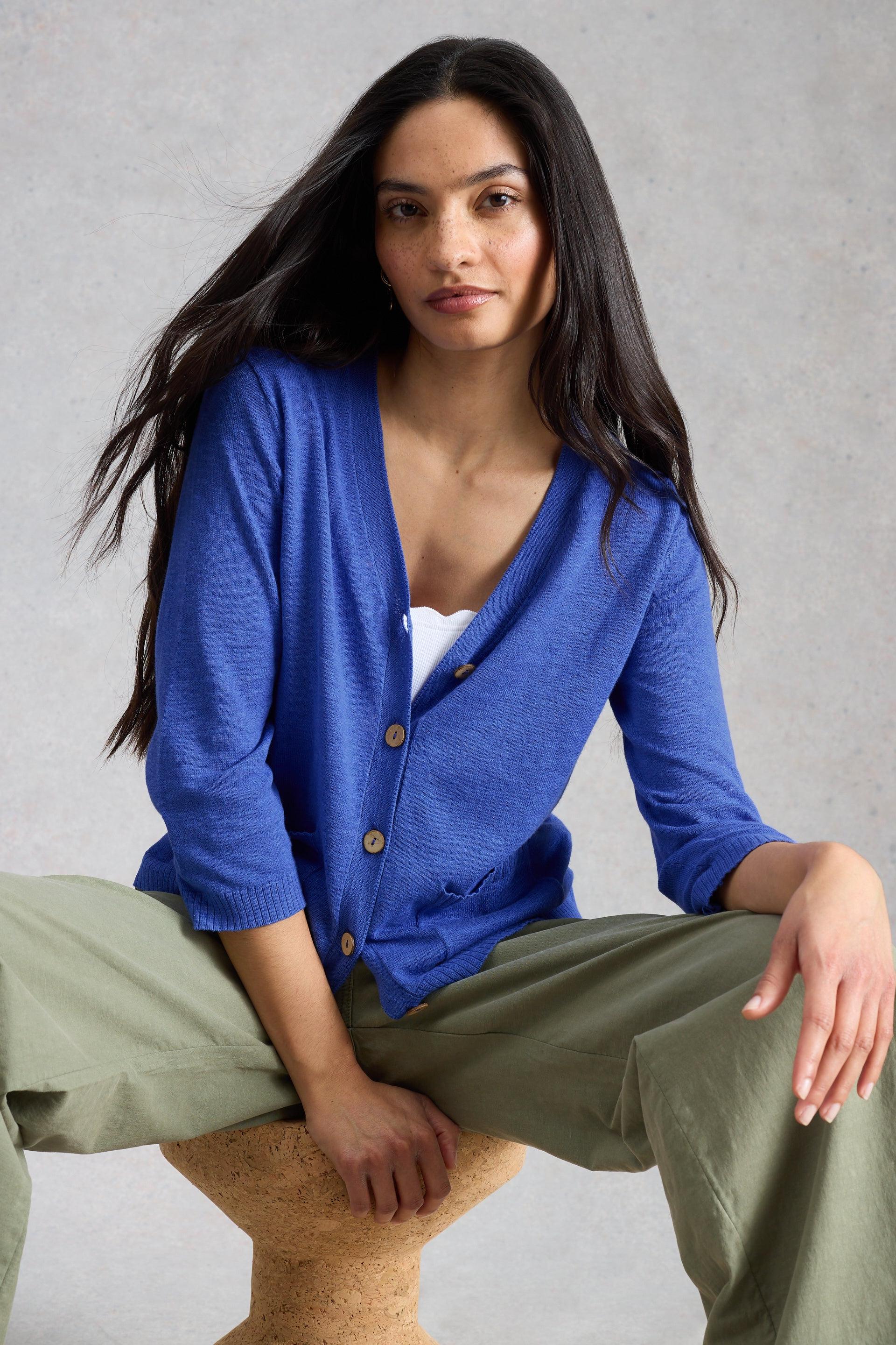 A woman with long dark hair wearing a blue organic cotton cardigan over a white top.