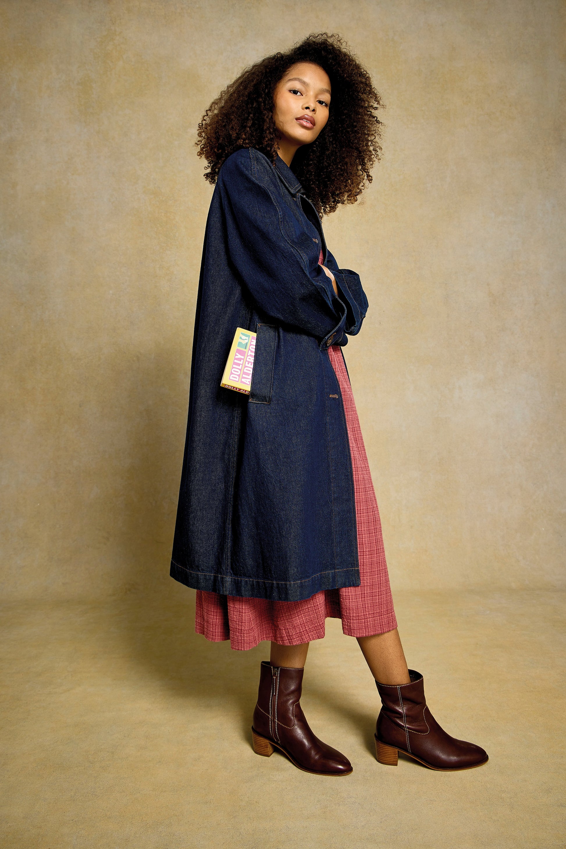 Woman with curly hair wearing a denim coat over a red organic cotton dress