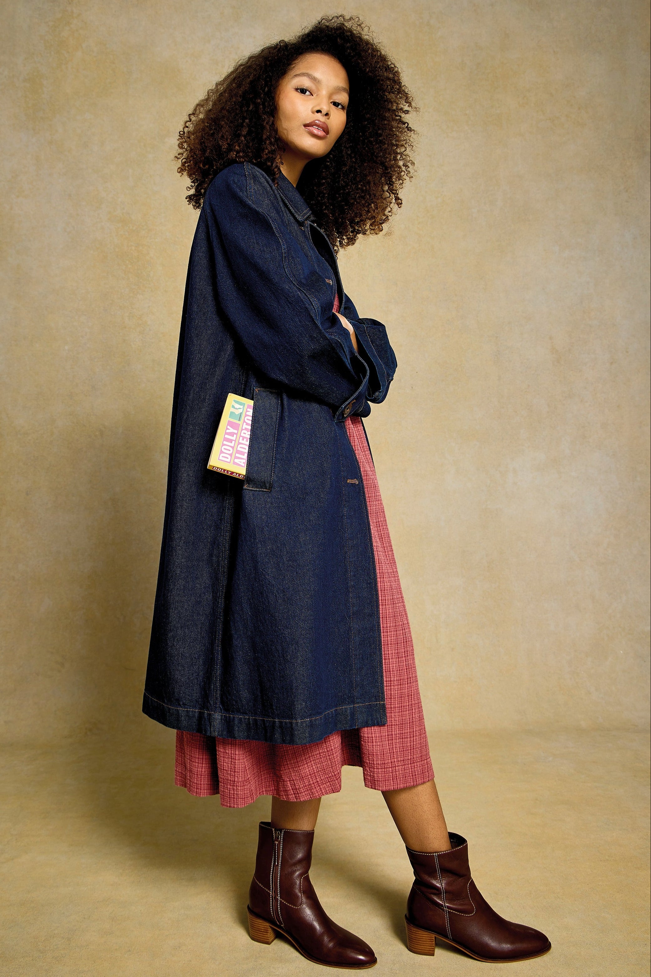 Woman with curly hair wearing a denim coat over a red organic cotton dress