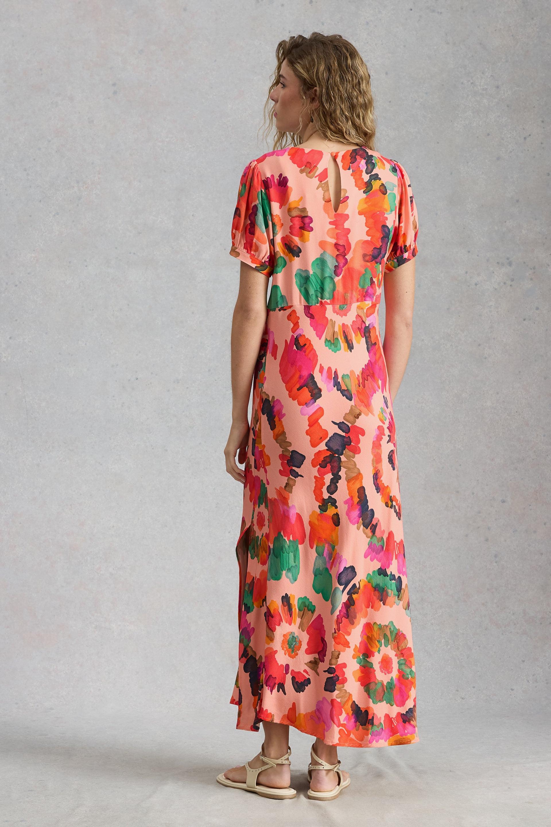 A woman wearing a vibrant pink floral occasion dress against a light grey studio background.