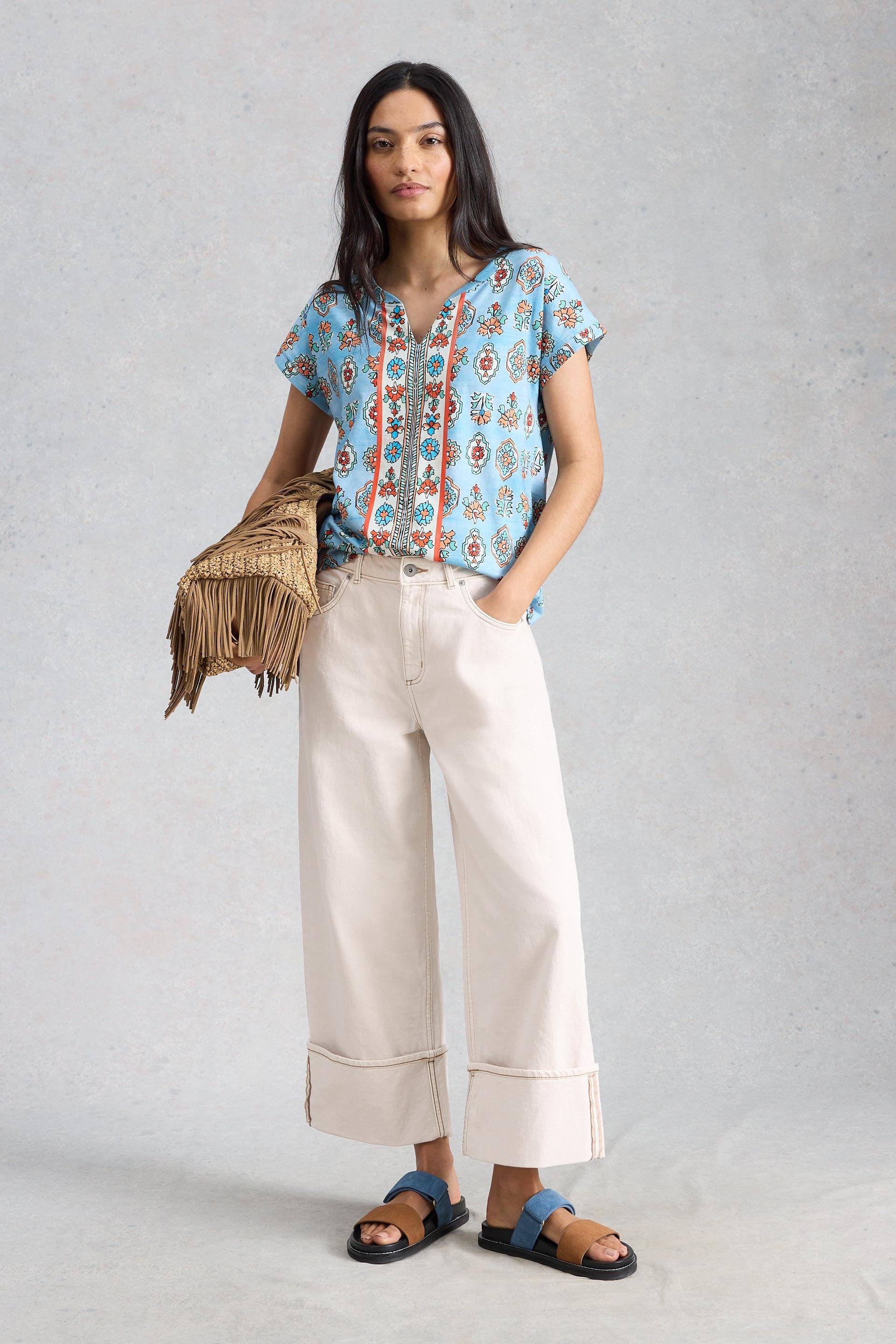 A woman wearing a blue floral patterned organic cotton top and wide-leg trousers from White Stuff.