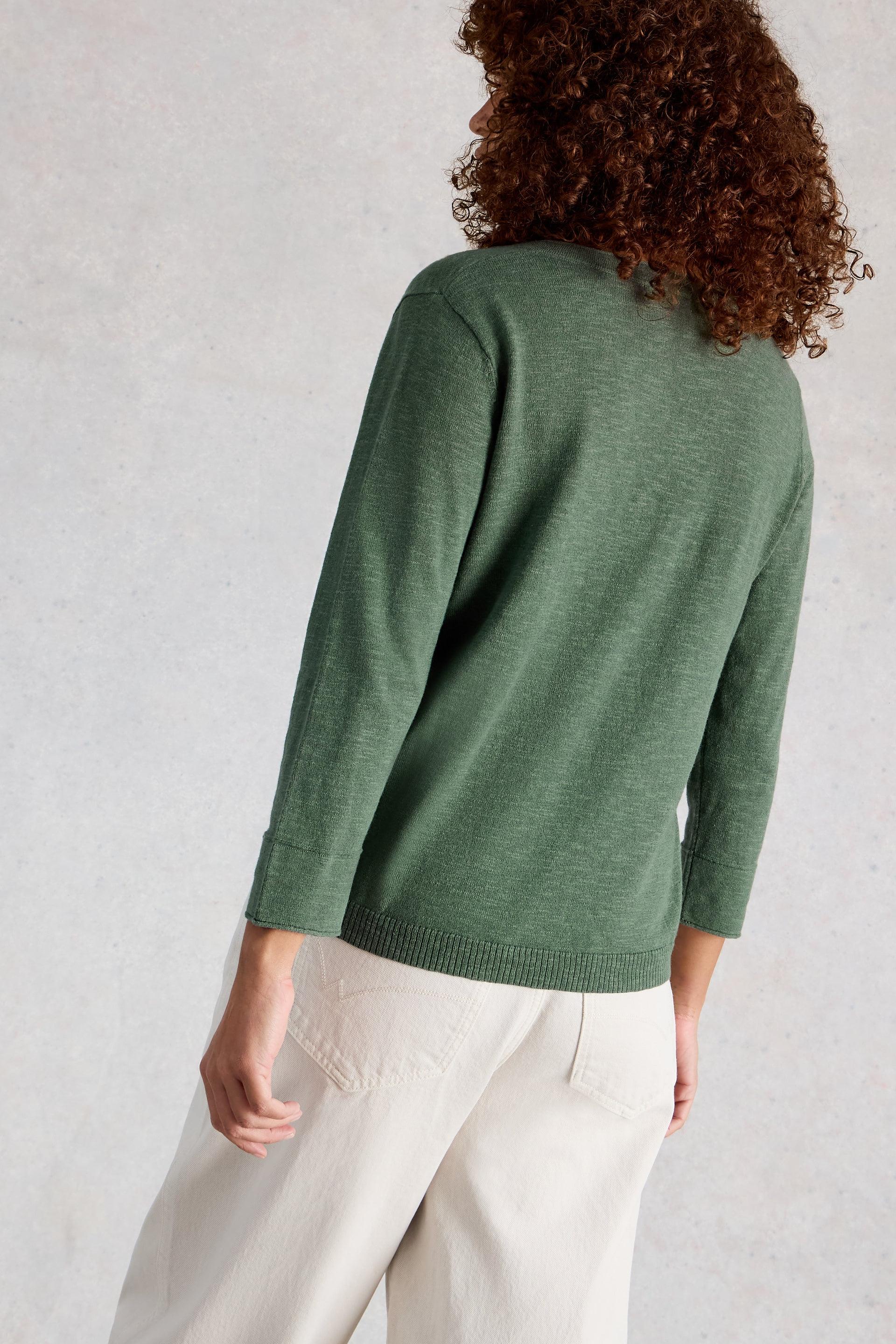 Woman wearing a green organic cotton V-neck sweater and white pants viewed from behind.