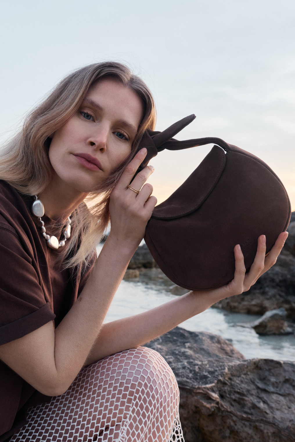 Woman holding a brown handbag by the water