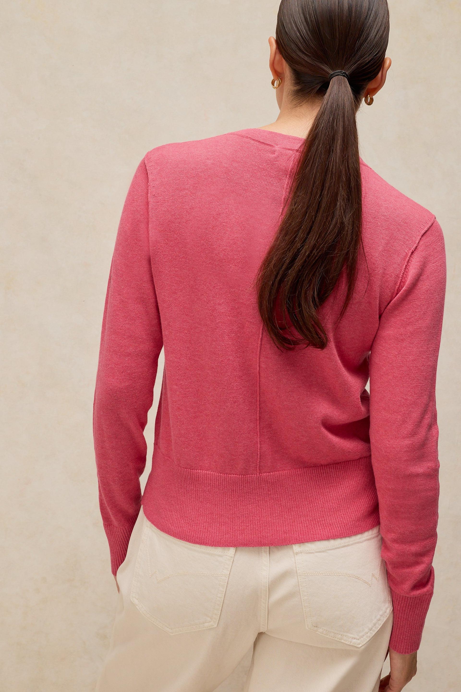 A woman seen from behind wearing a pink organic cotton sweater and white pants