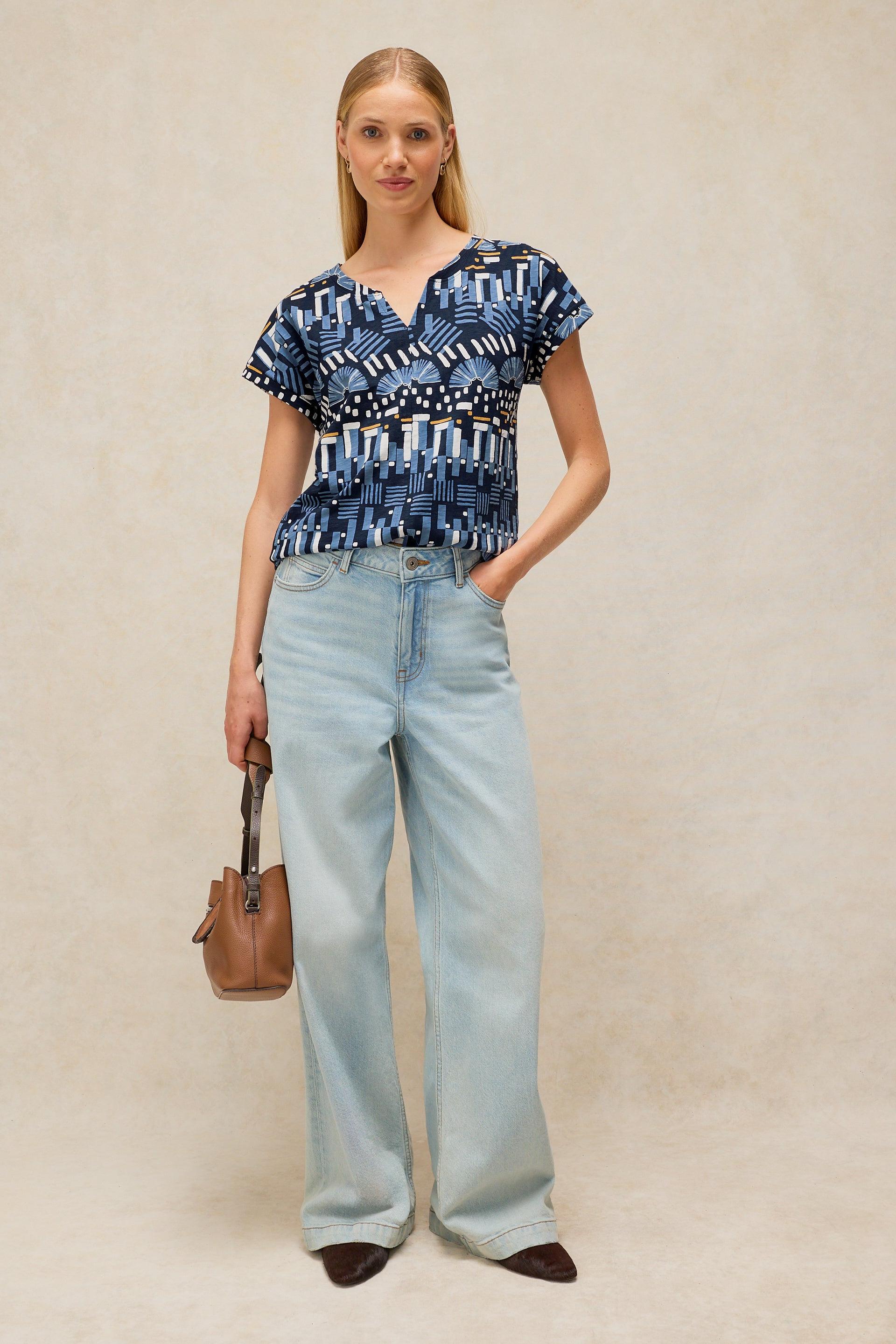 A woman posing in a navy blue patterned cotton top and light wash wide-leg denim jeans