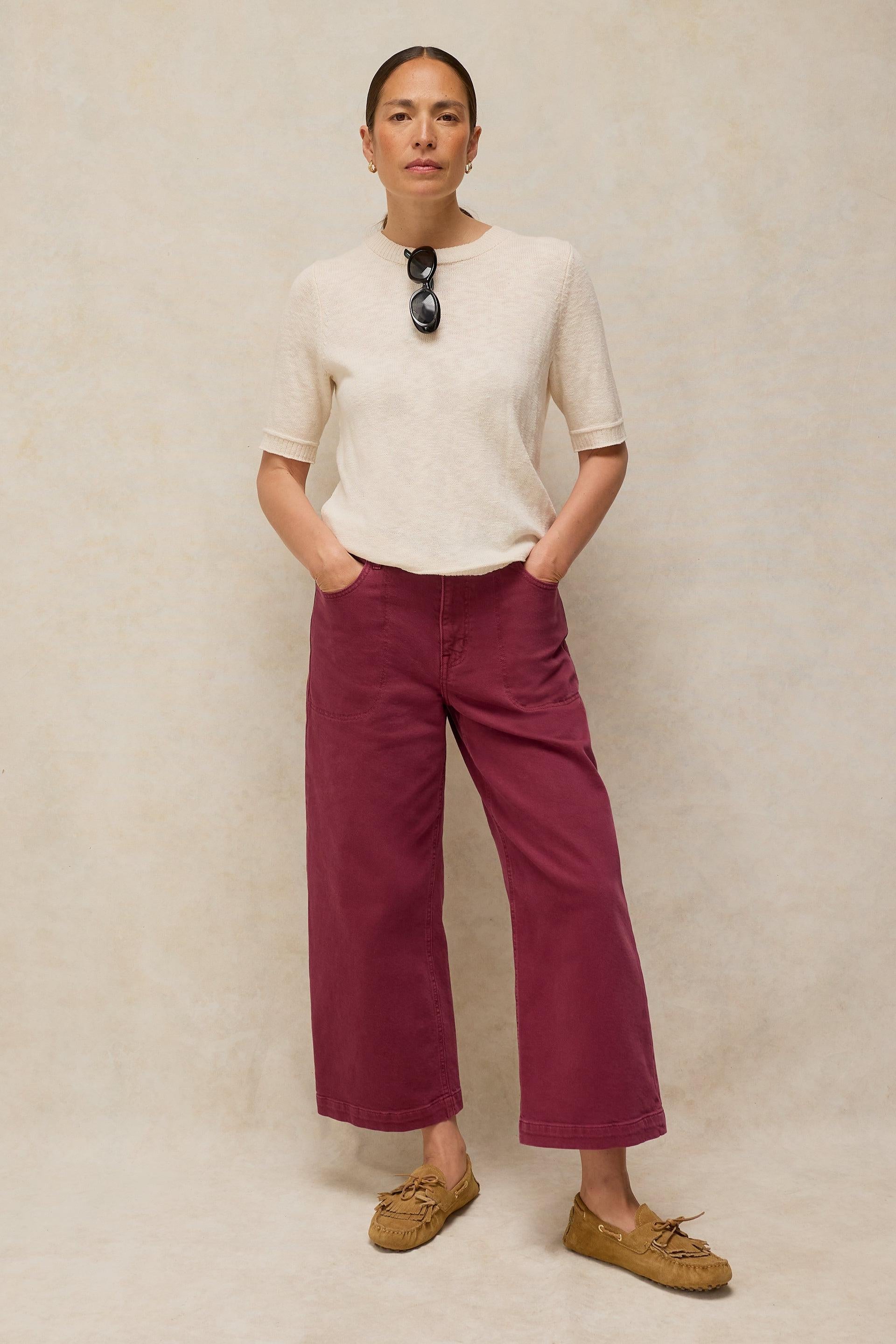 Woman wearing an organic cotton white t-shirt and burgundy trousers standing against a textured backdrop