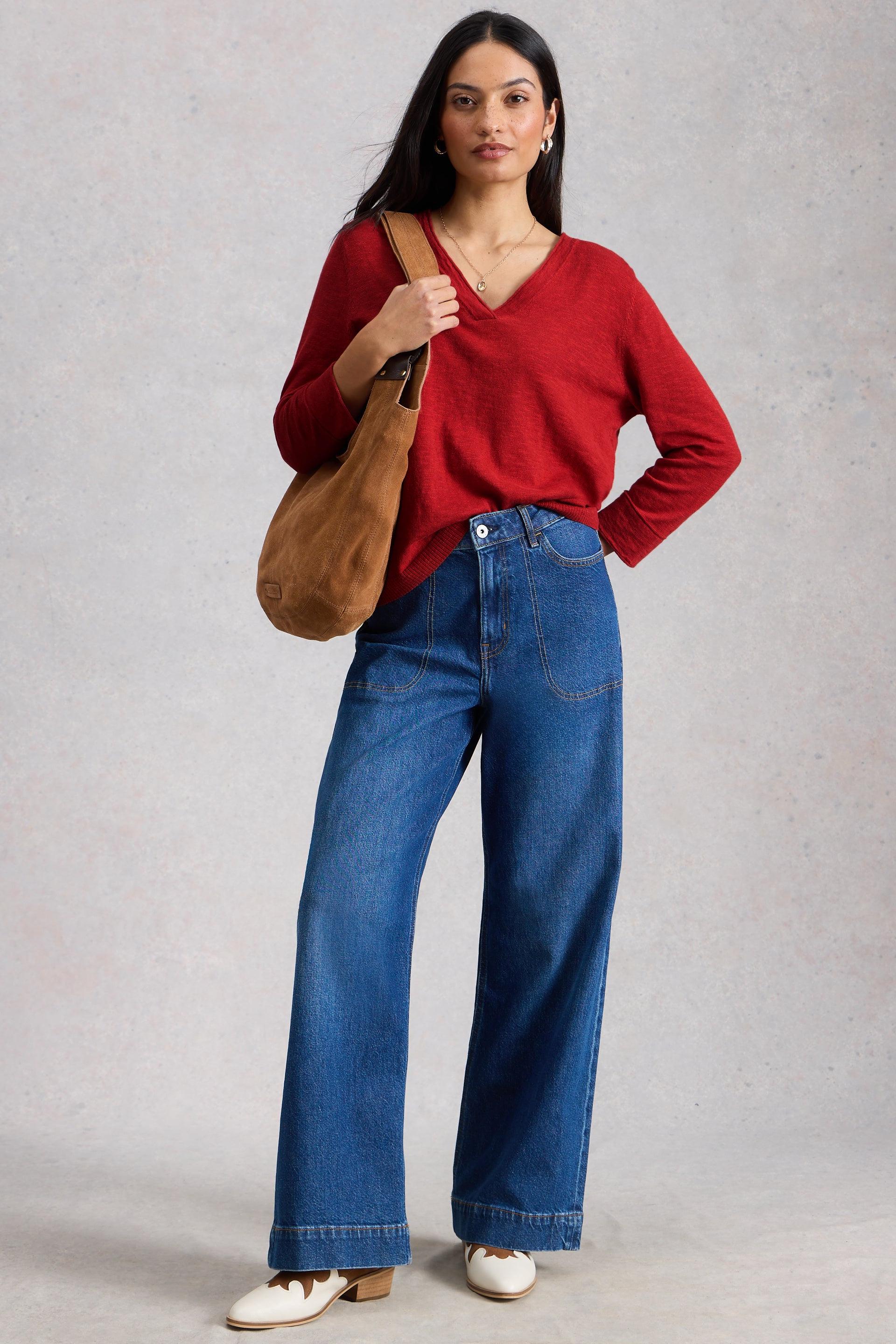 A woman wearing a red v-neck organic cotton sweater and wide-leg blue jeans with a brown suede bag.