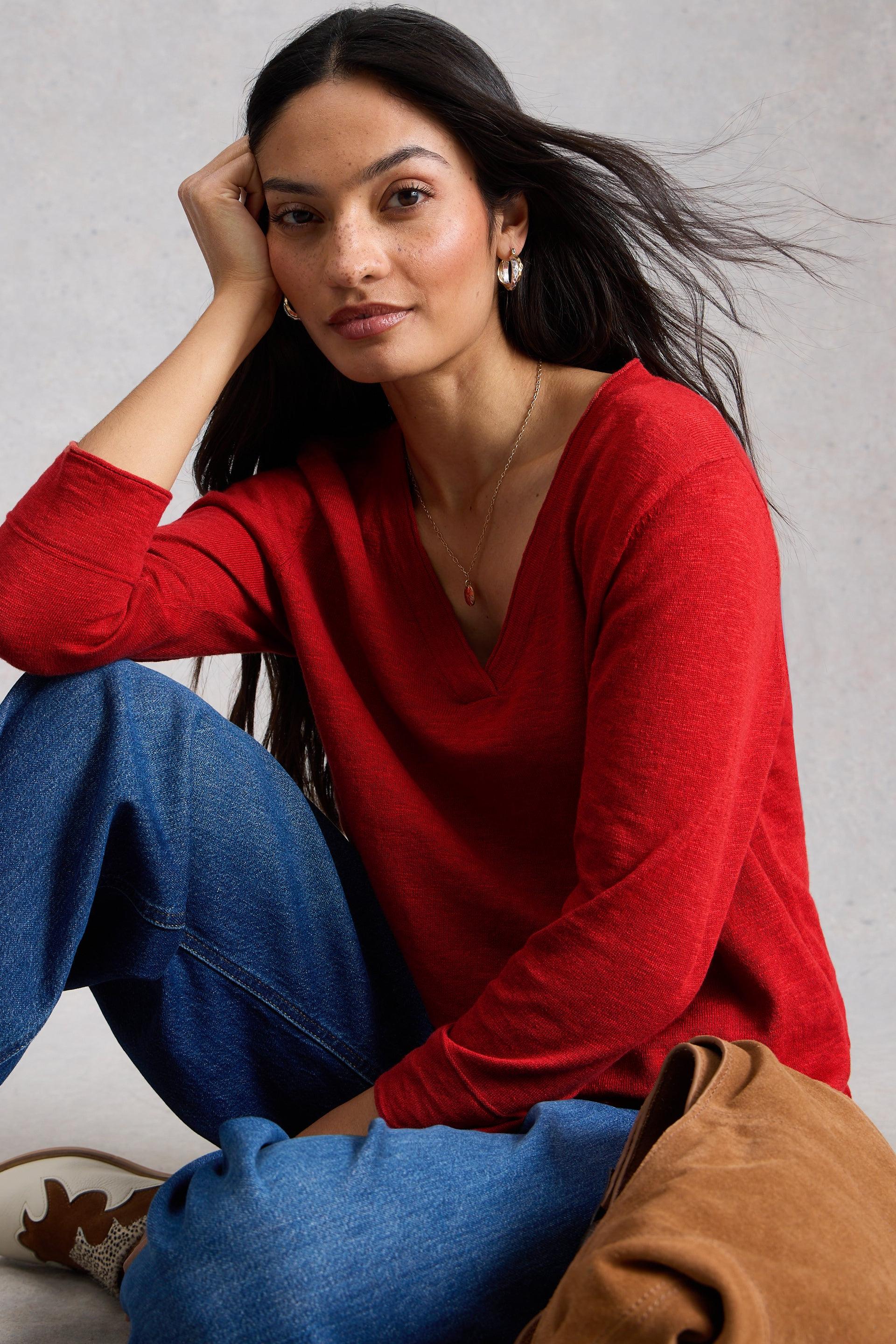 Woman sitting wearing a red v-neck sweater made of organic cotton.