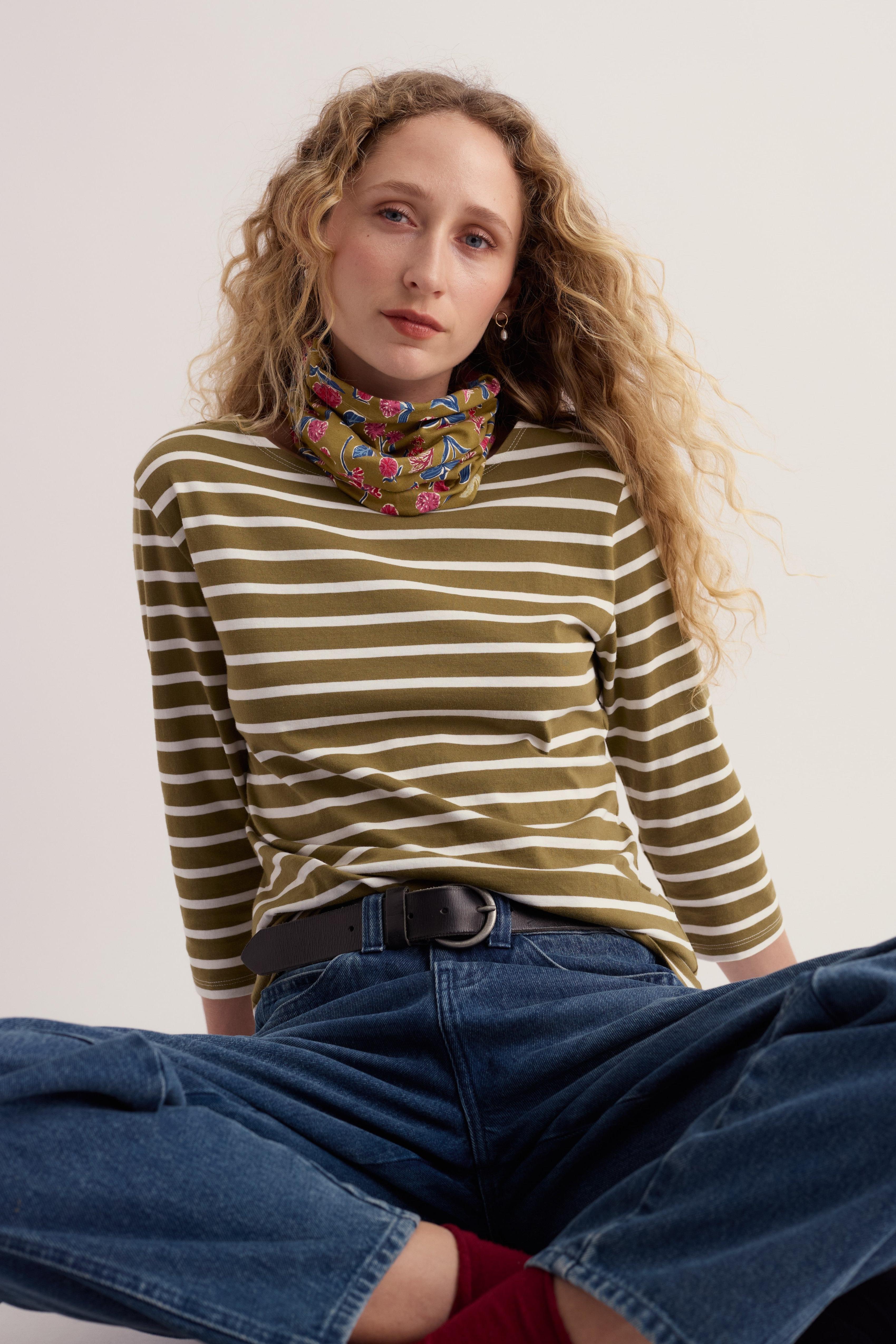 Woman with curly blonde hair wearing a striped organic cotton long-sleeve top and blue jeans