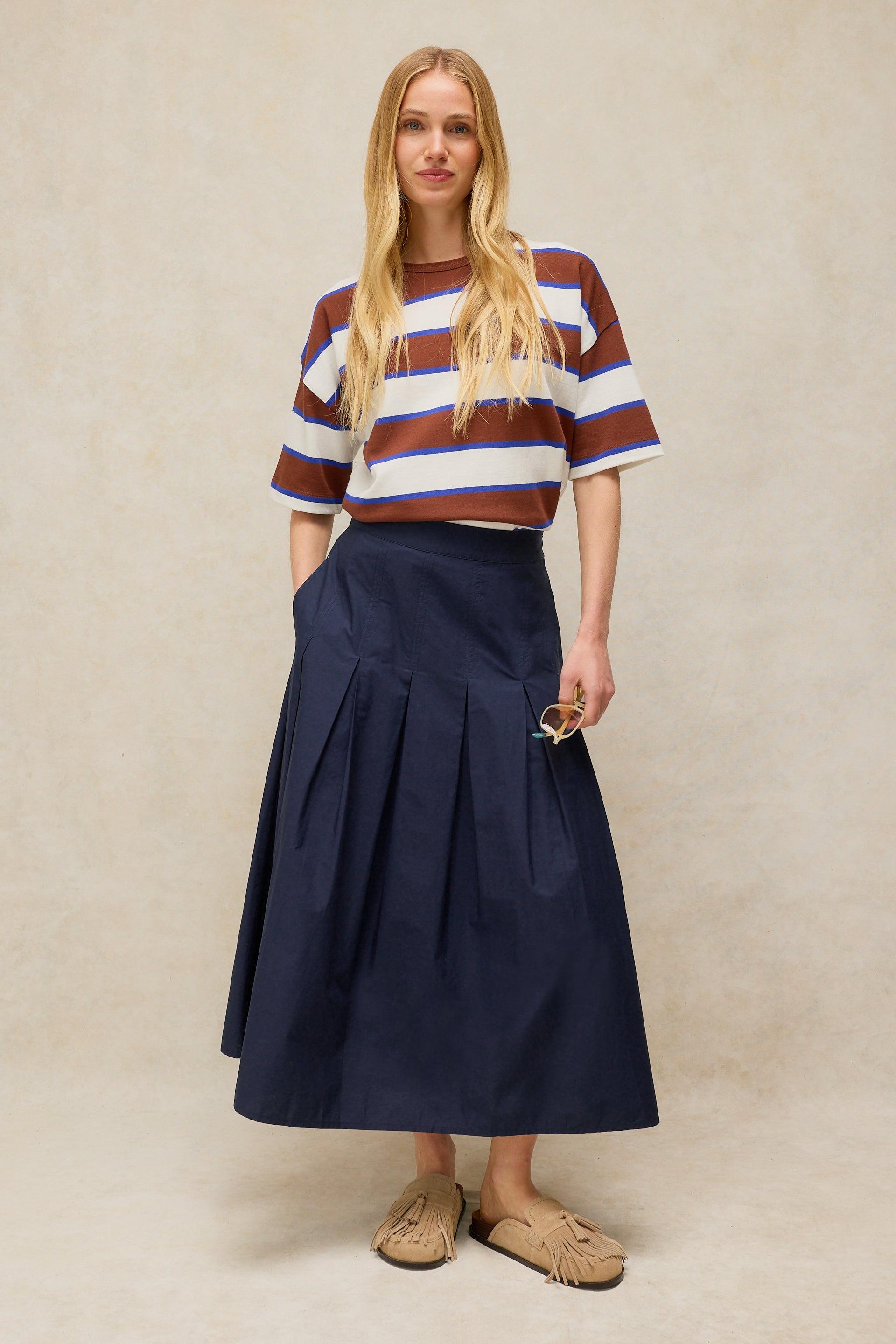 Blonde woman wearing a striped t-shirt and navy pleated midi skirt from White Stuff in organic cotton
