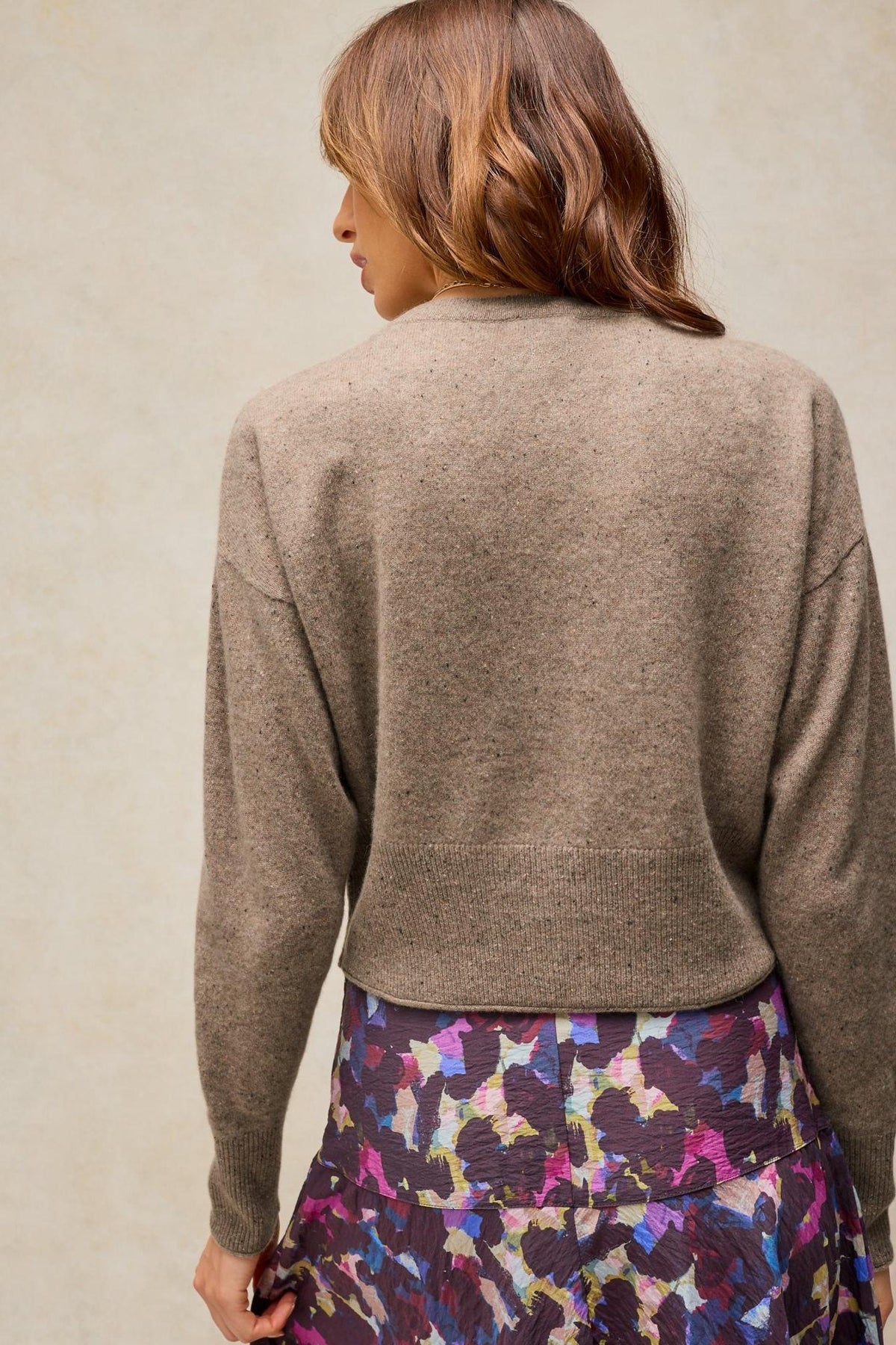 A woman seen from behind wearing a natural coloured cashmere knit cardigan over a patterned skirt.