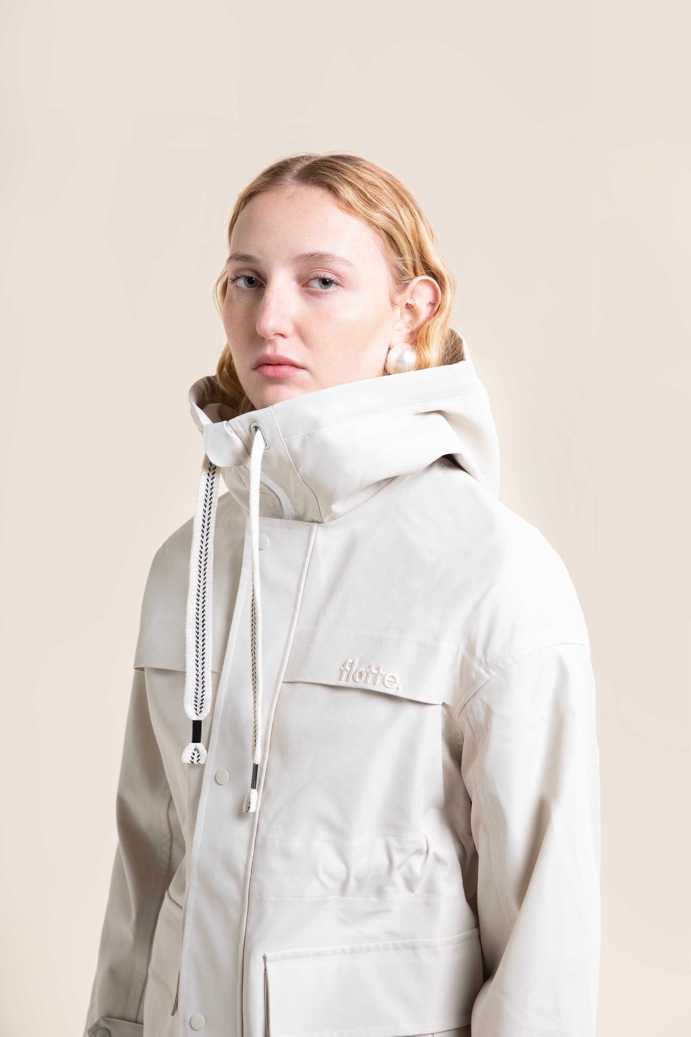 A woman wearing a stylish beige Flotte waterproof coat against a neutral background.