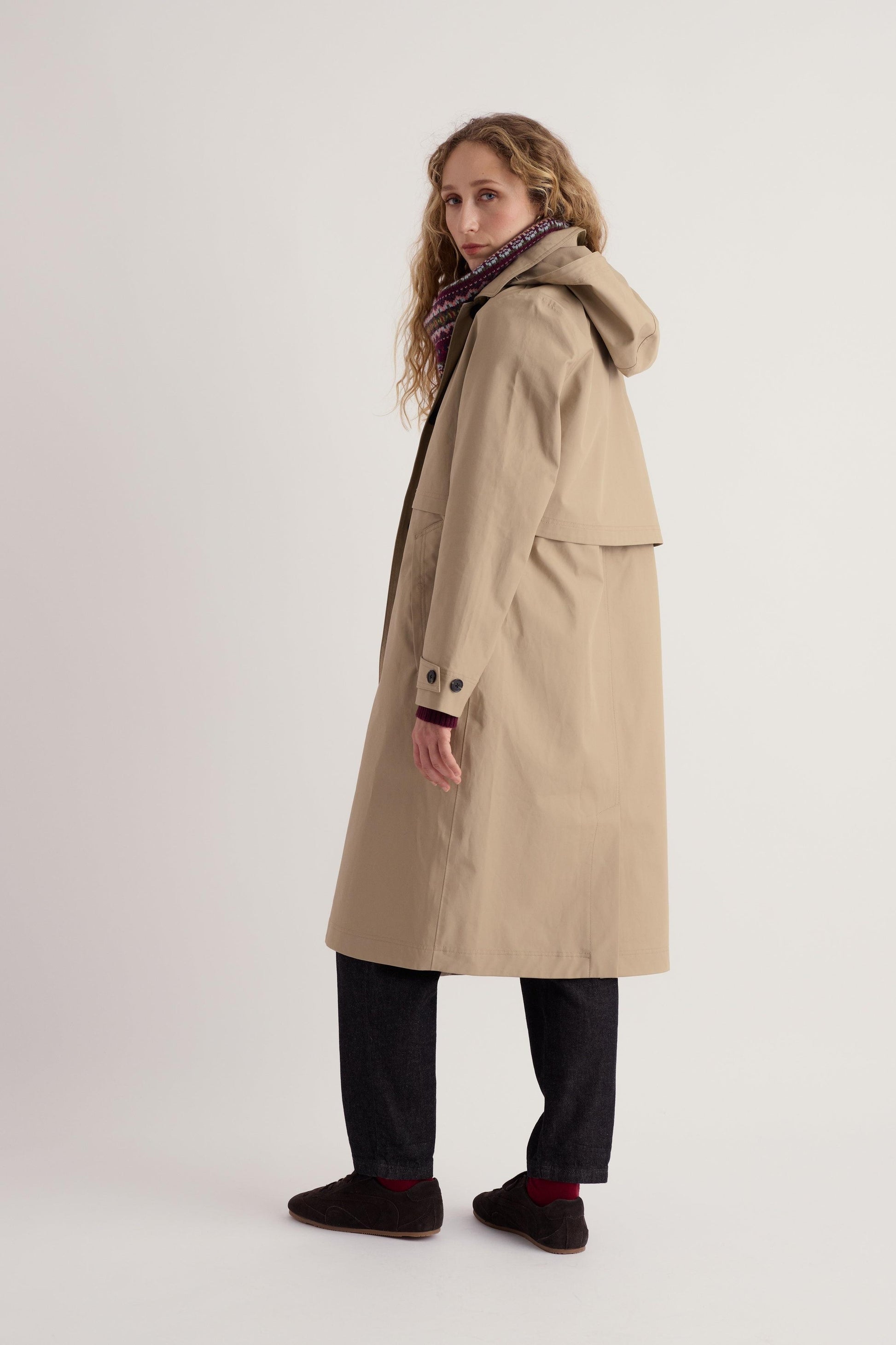 A woman wearing a beige waterproof trench coat from Seasalt Cornwall against a plain studio background.