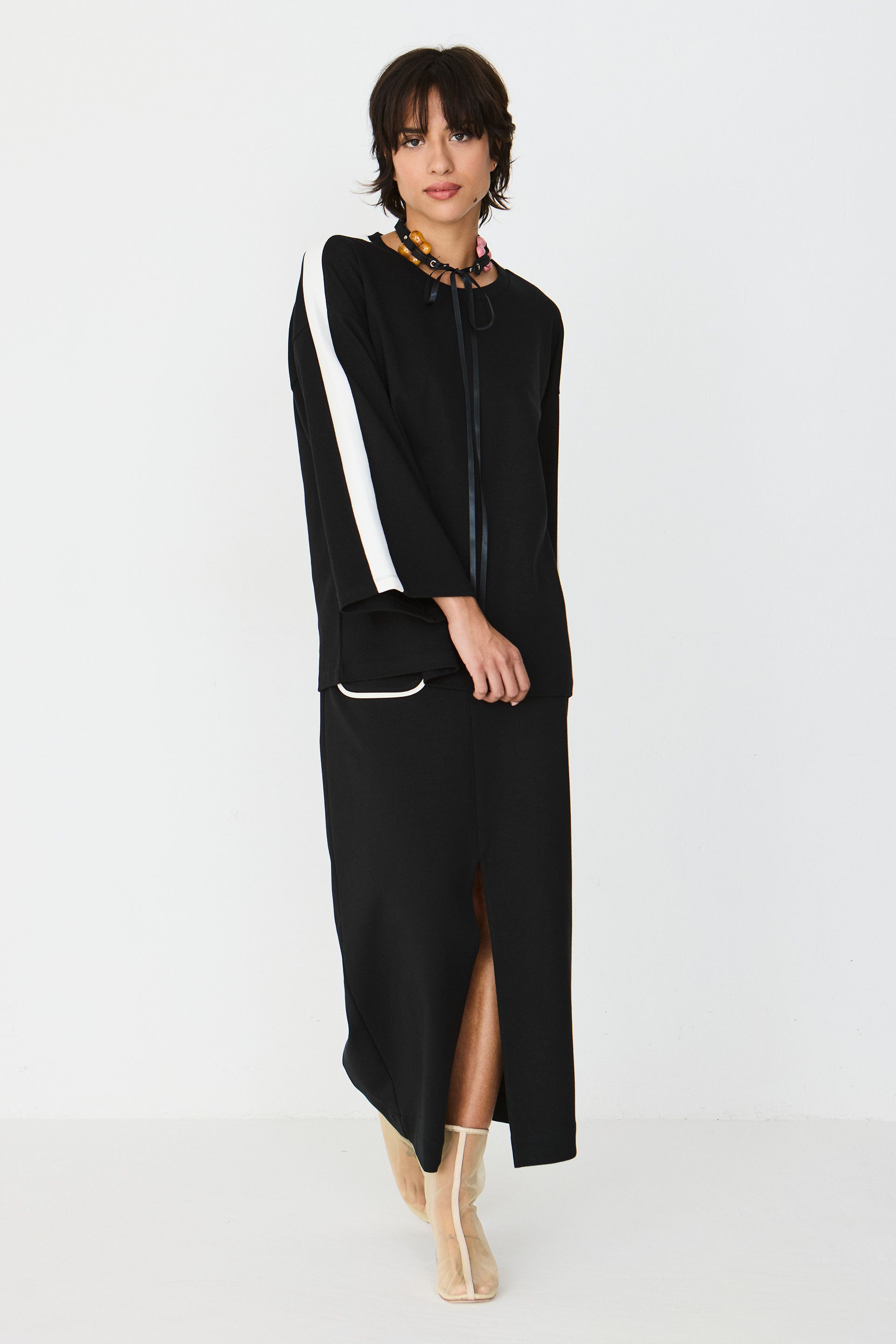 A woman posing in a black long-sleeved top and matching midi skirt with white side accents and sheer boots