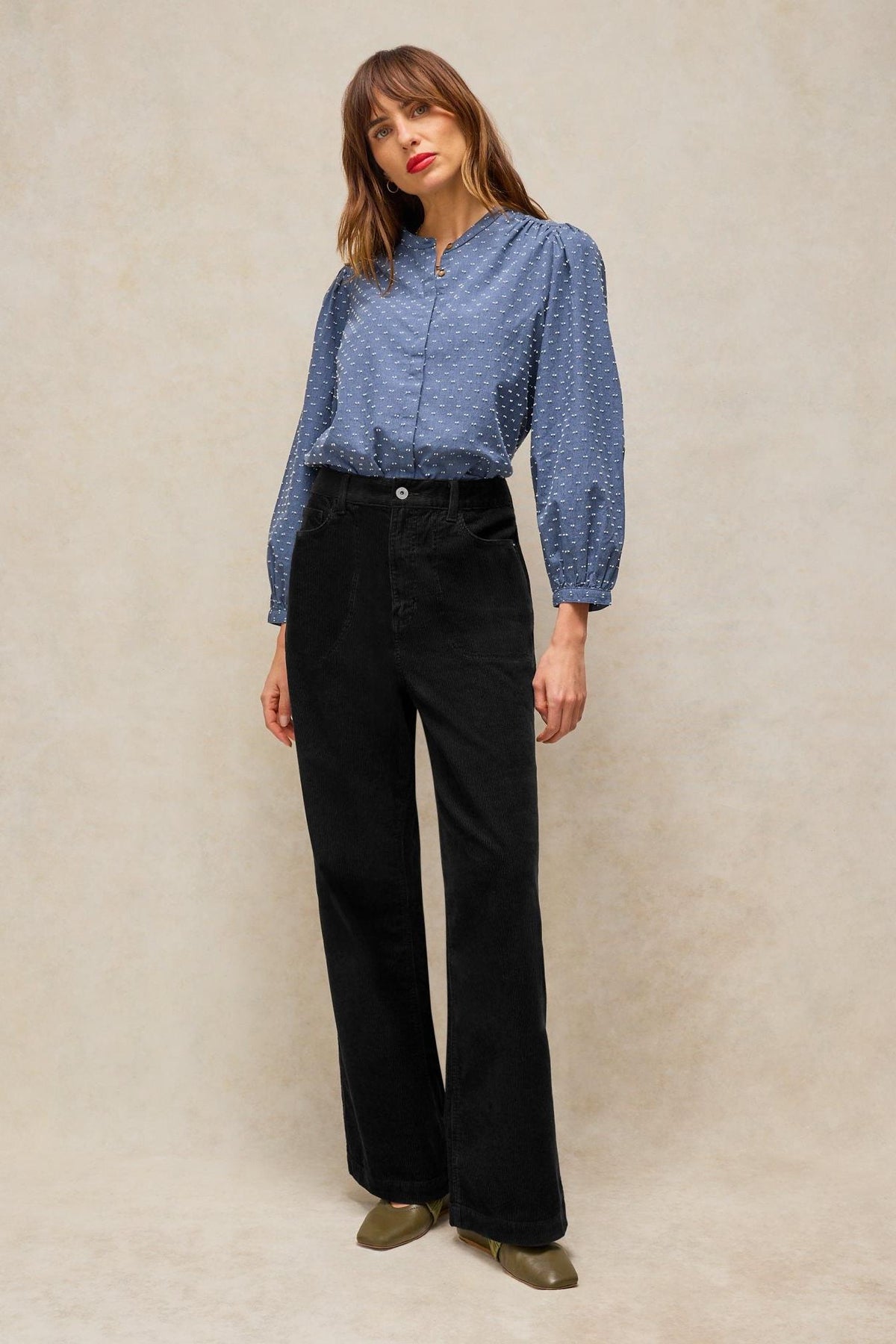 Woman modeling casual black cord wide leg trousers and a patterned blue long-sleeved blouse.
