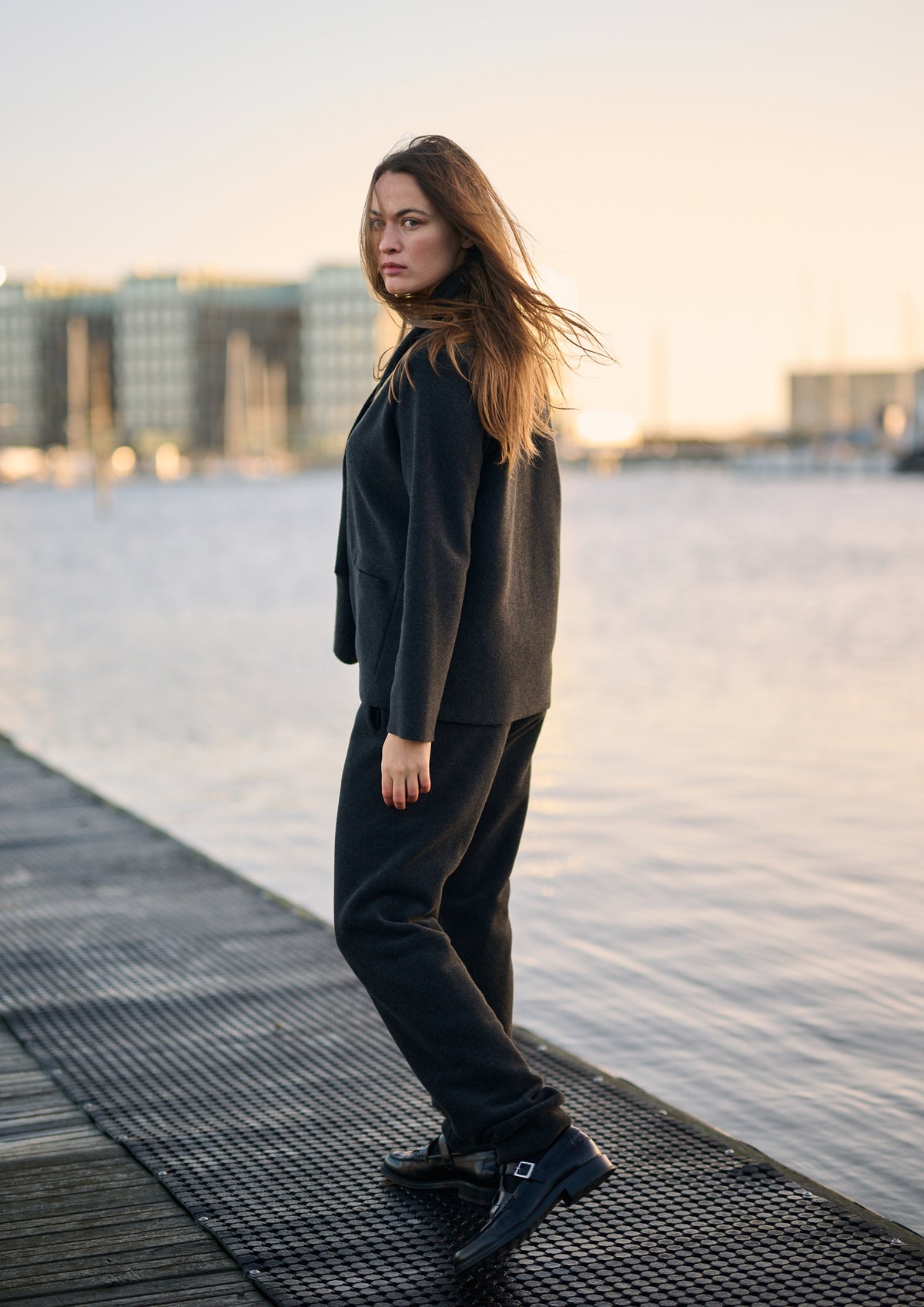 Woman in a black fleece cardigan posing on a wooden pier at sunset