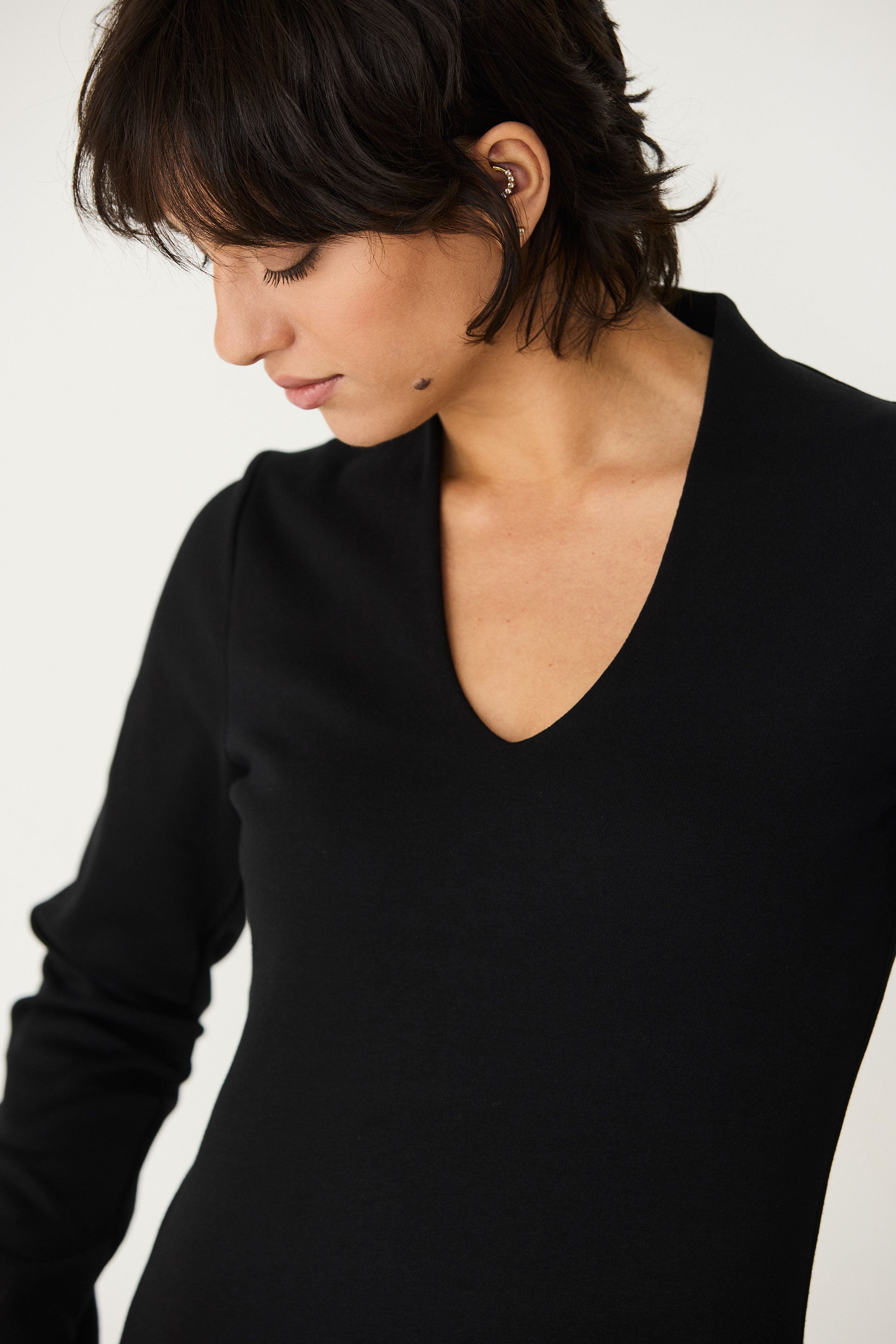 A woman with short dark hair wearing a black long sleeve organic cotton top with a V-neckline.