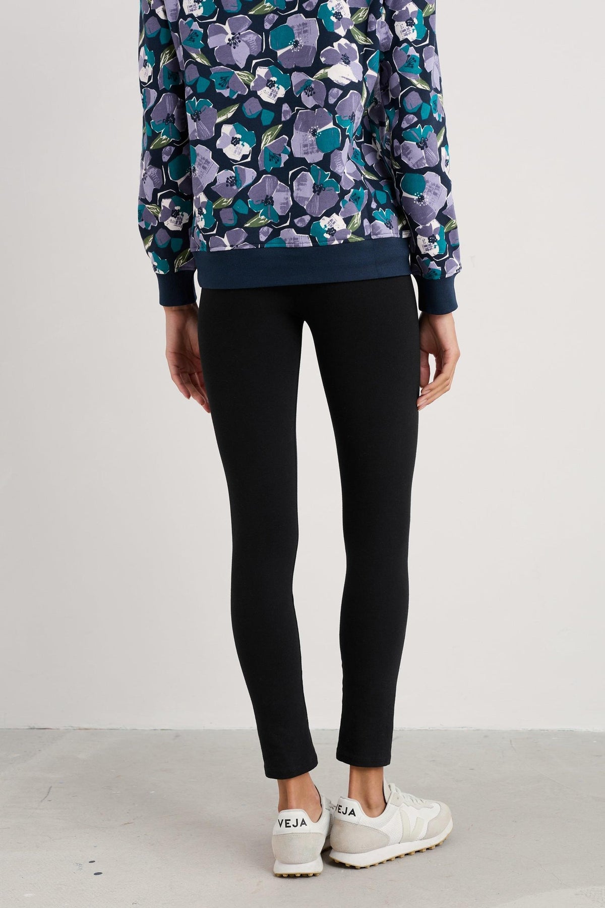 Woman standing from behind wearing fitted black organic cotton leggings and a floral print top.