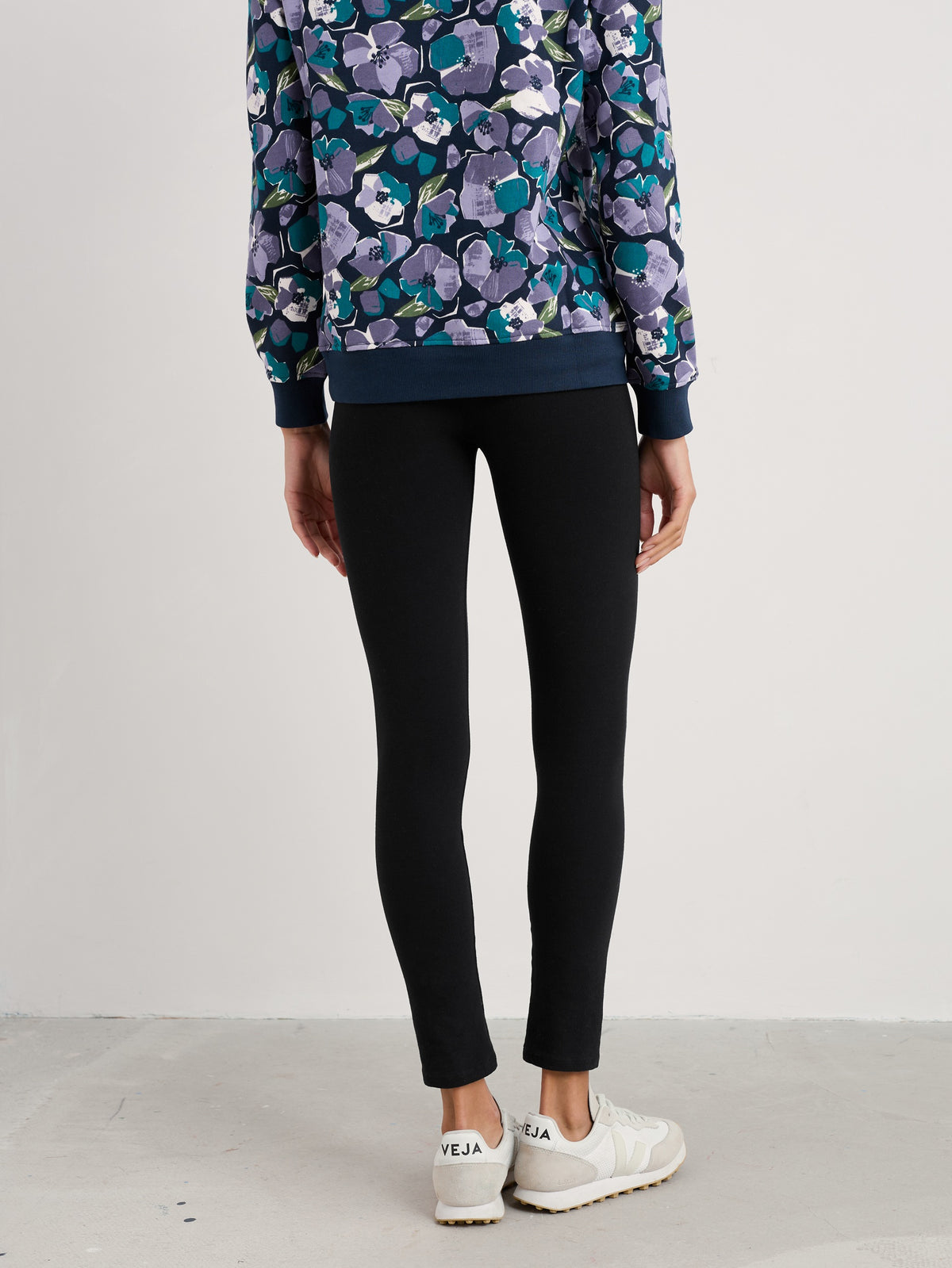 Woman standing from behind wearing fitted black organic cotton leggings and a floral print top.