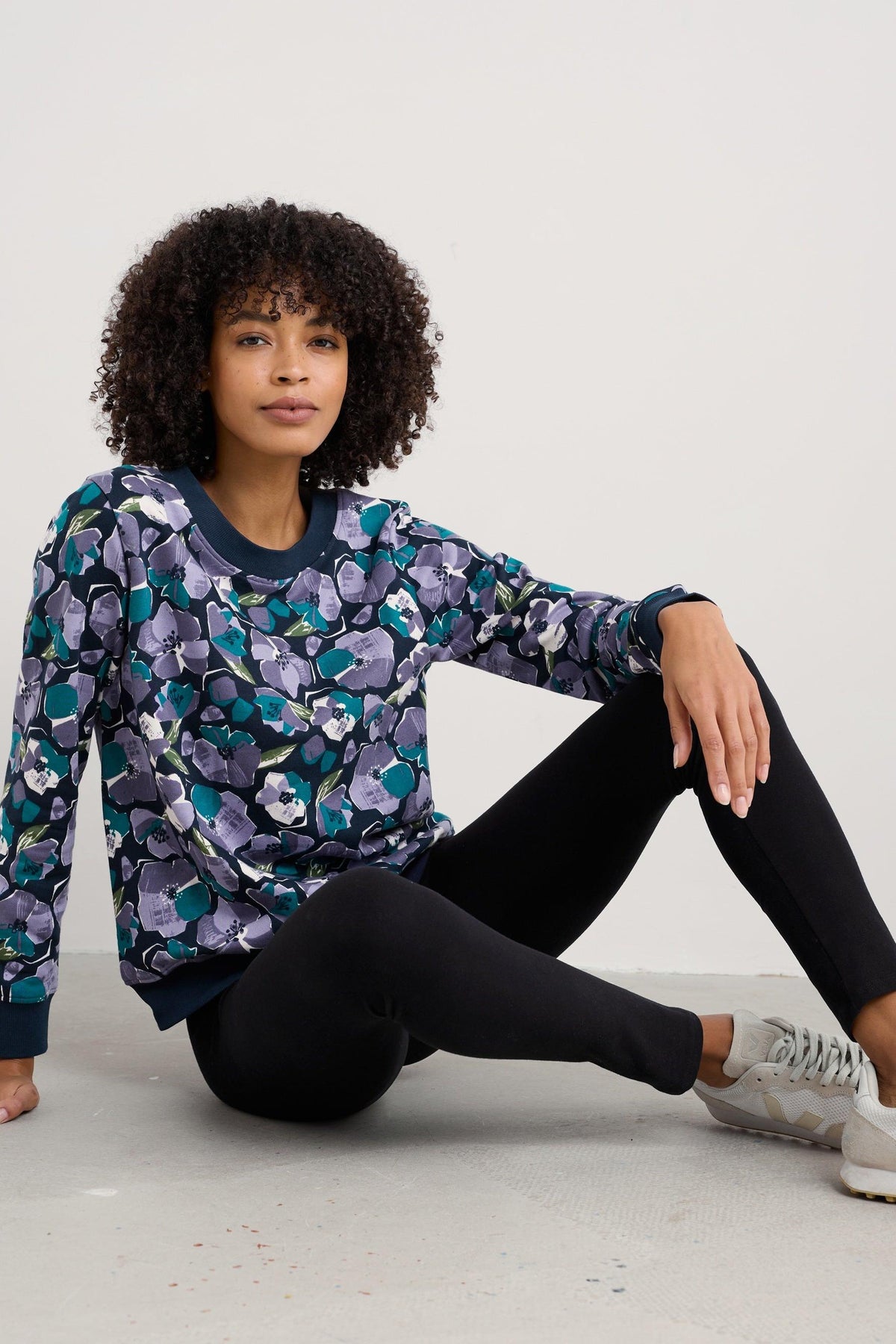 A woman sitting on the floor wearing a floral patterned sweatshirt and black Seasalt Cornwall leggings.