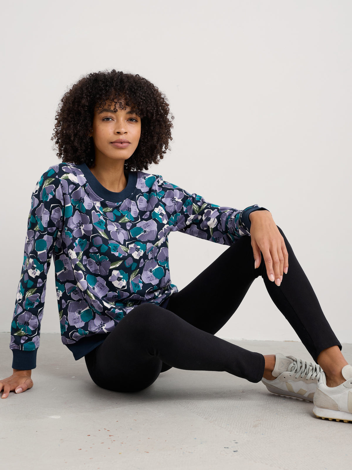 A woman sitting on the floor wearing a floral patterned sweatshirt and black Seasalt Cornwall leggings.