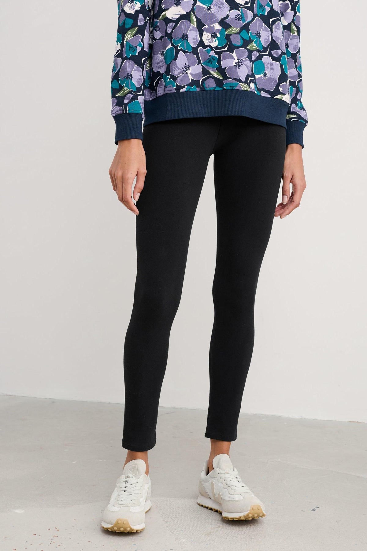 Woman standing wearing black Seasalt Cornwall organic cotton leggings paired with white sneakers.